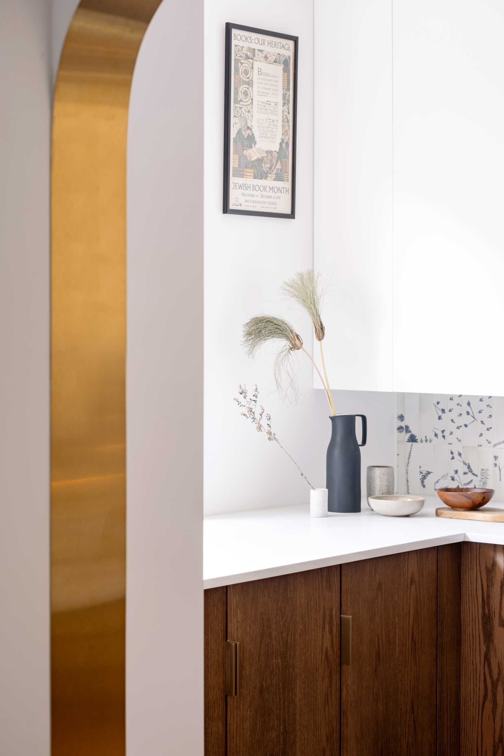 A modern kitchen with dark wood and white cabinets, white countertops, Dutch “Delft” tile, and brass-lined arches.