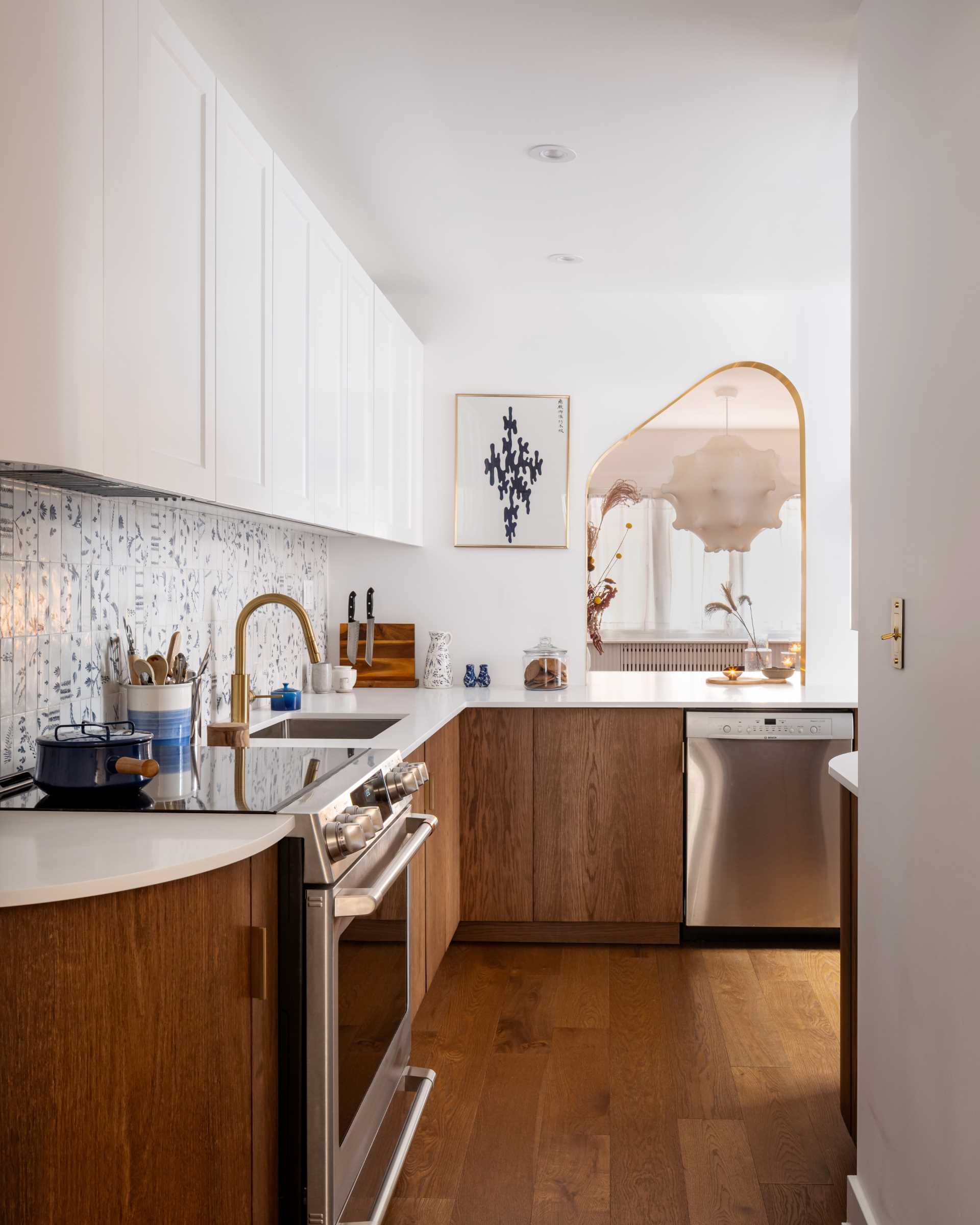 A modern kitchen with dark wood and white cabinets, white countertops, Dutch “Delft” tile, and brass-lined arches.