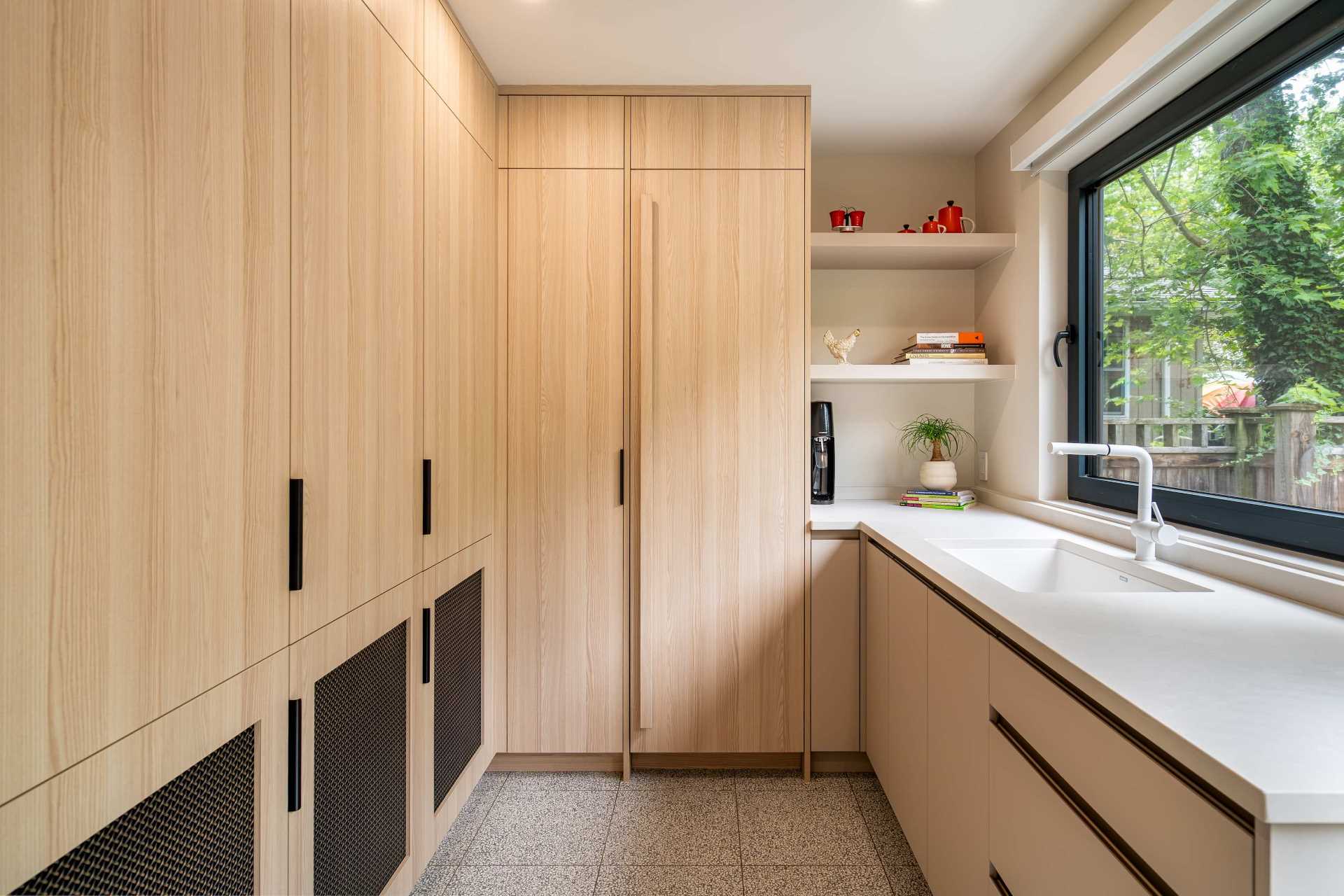 A hidden walk-in pantry is located behind a door with a mesh screen and includes an abundance of storage, additional counter space, and a sink.