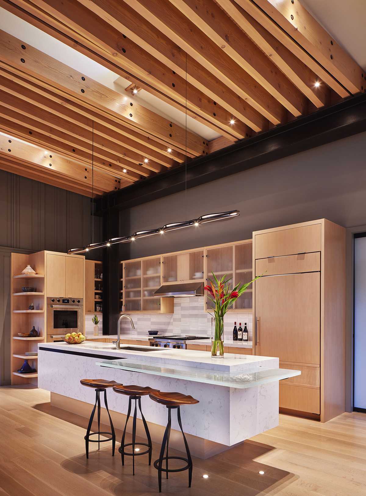 In the kitchen, European beech cabinets and white-stained oak floors are combined with serene grey walls. The kitchen island is a sculptural accent piece in white quartzite, with a cast-glass breakfast counter supported by a laser-cut steel panel.