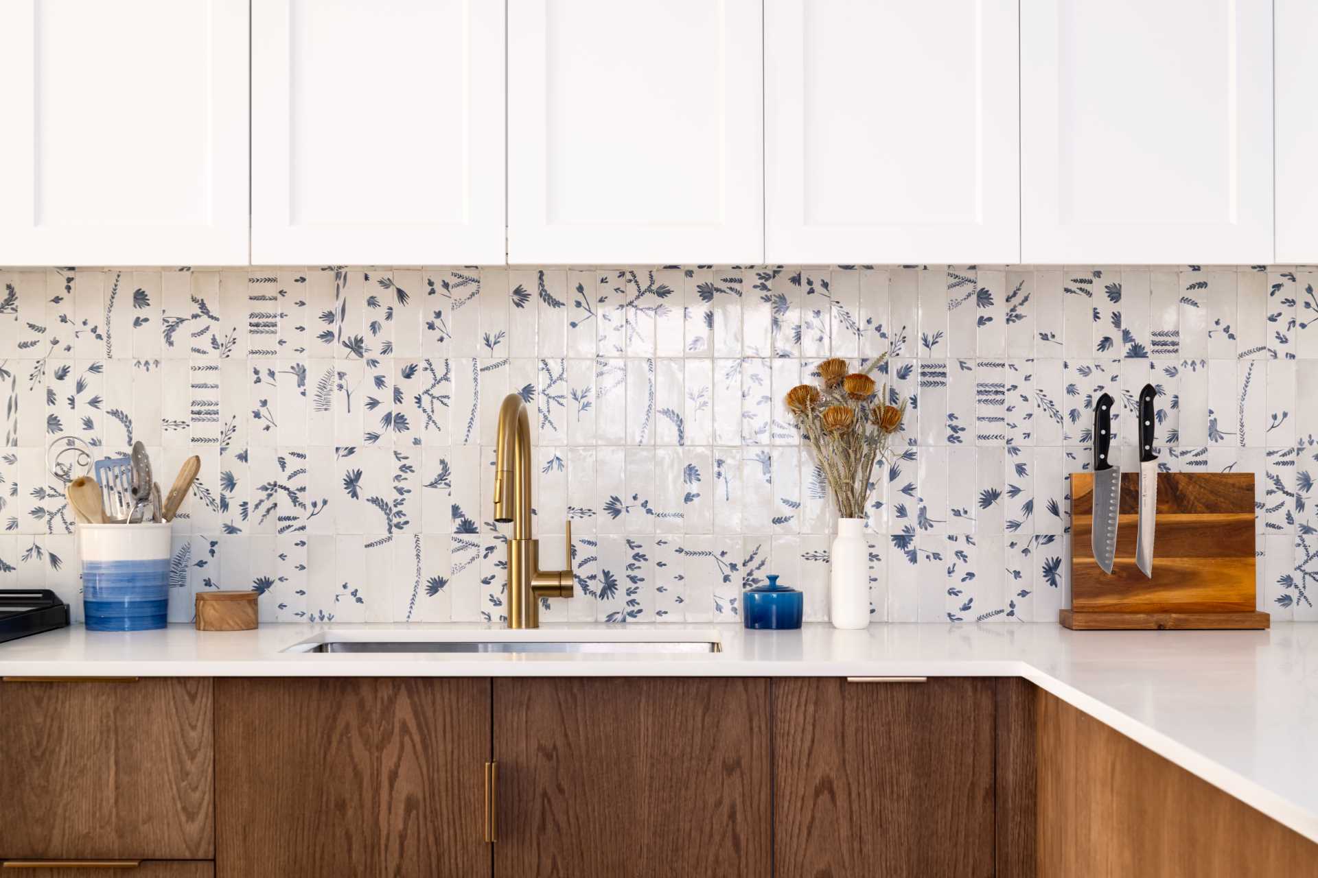 A modern kitchen with dark wood and white cabinets, white countertops, Dutch “Delft” tile, and brass accents.