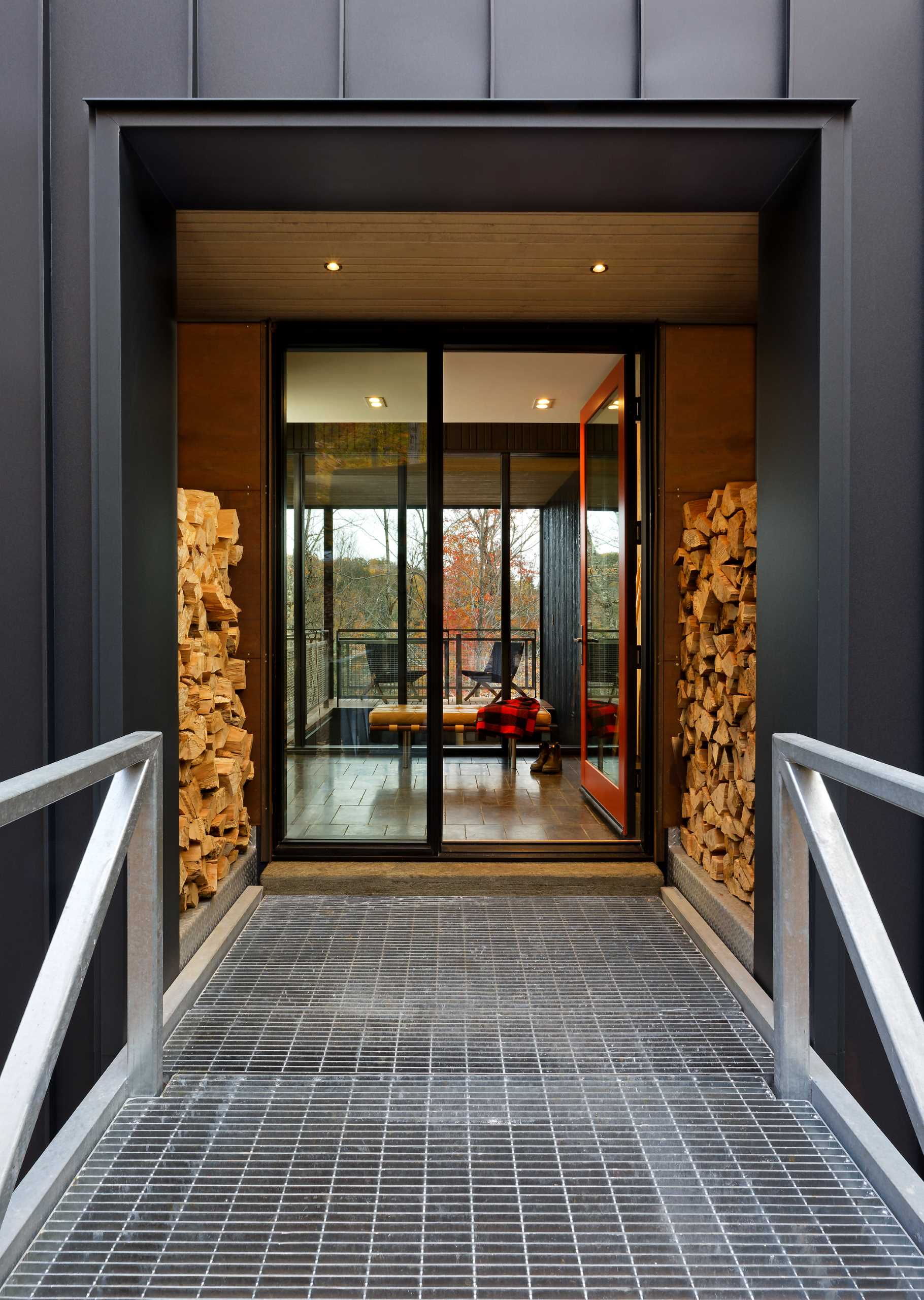 A galvanized steel bridge, which connects the granite slab steps of the hillside, brings you across to the generous glazed front doorway, while the dark exterior material palette allows the home to contrast the lively colors of the forest.