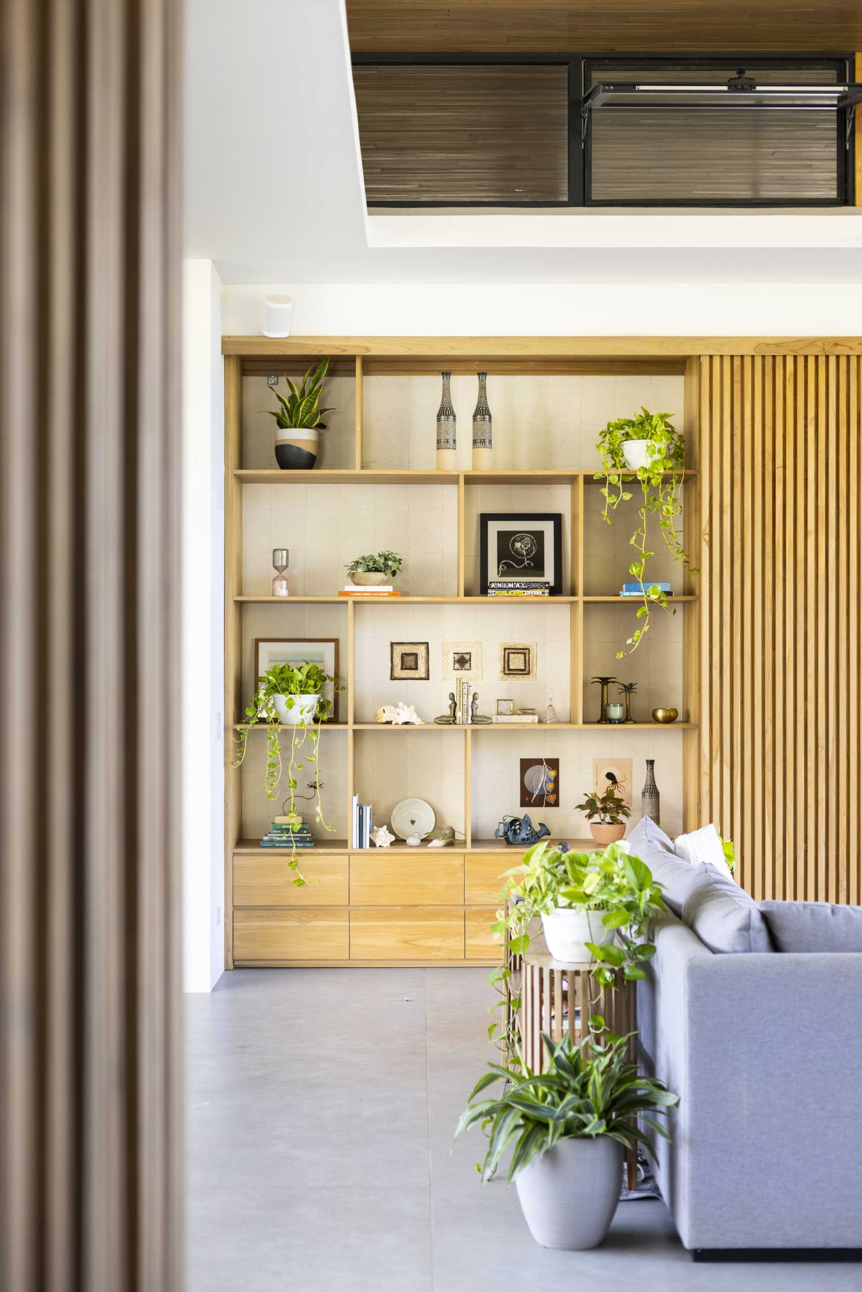 Inside, the living room and kitchen share the same large space, with clerestory windows, custom shelving, and openings to outdoor areas.