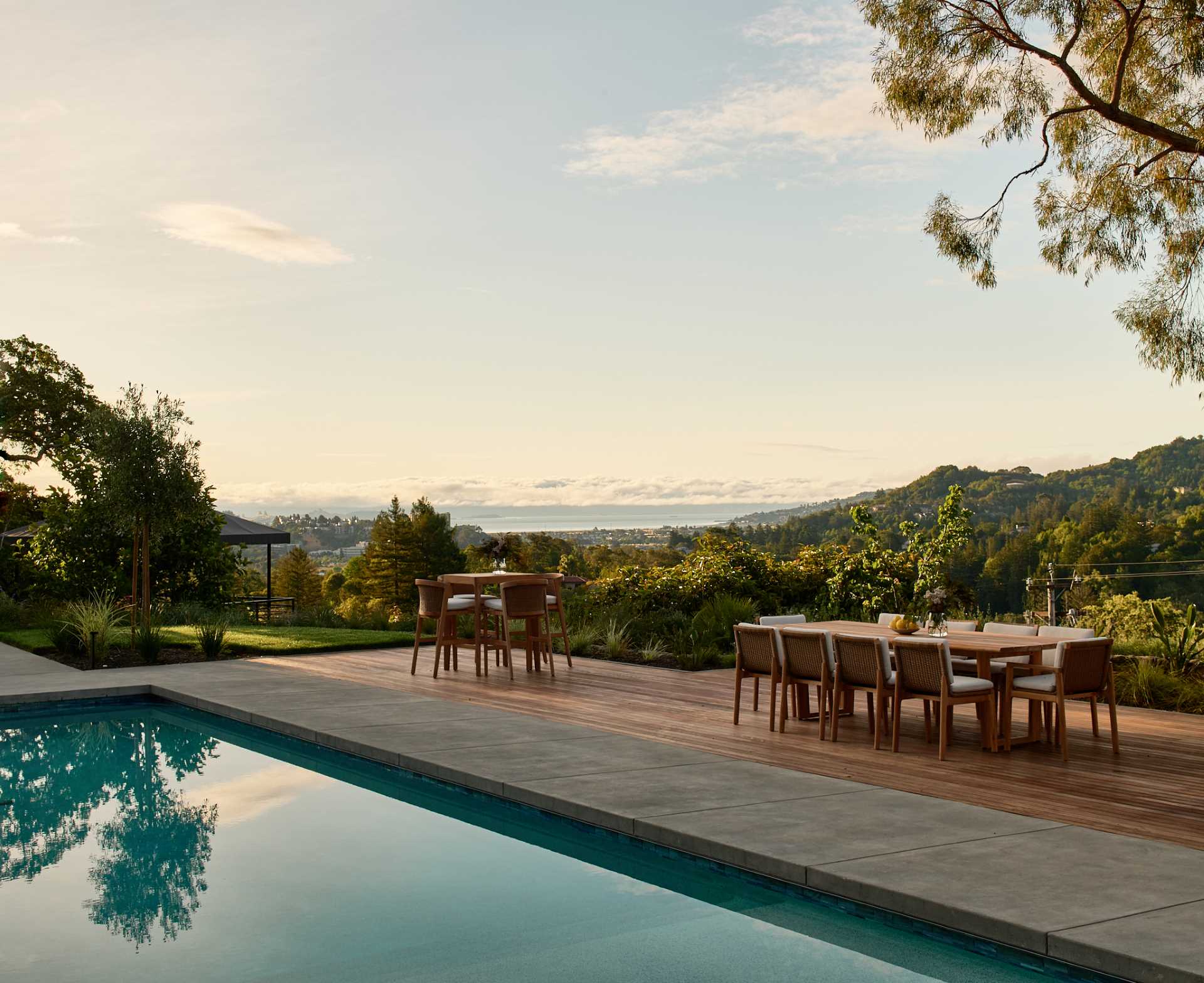 A pool surrounded by a deck includes spaces for dining and lounging, and a pool house provides a shaded space.