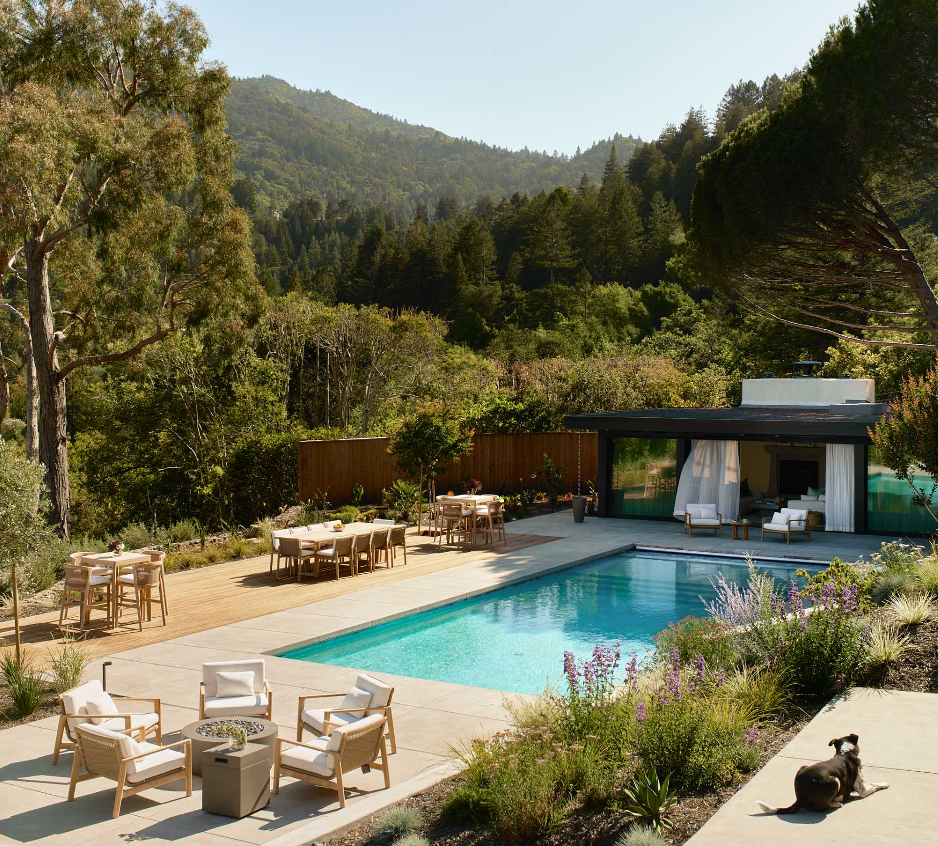 A pool surrounded by a deck includes spaces for dining and lounging, and a pool house provides a shaded space.