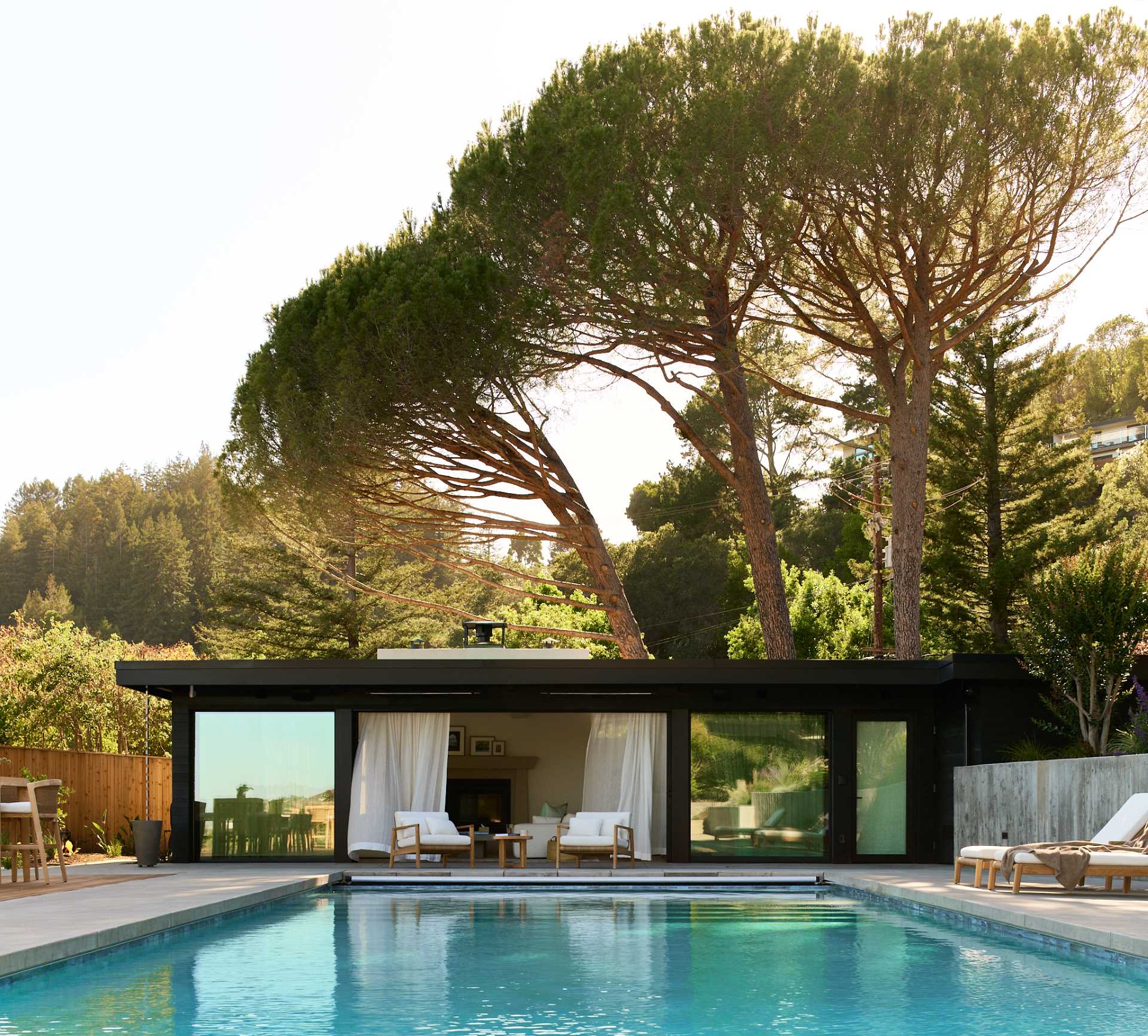 A pool surrounded by a deck includes spaces for dining and lounging, and a pool house provides a shaded space.