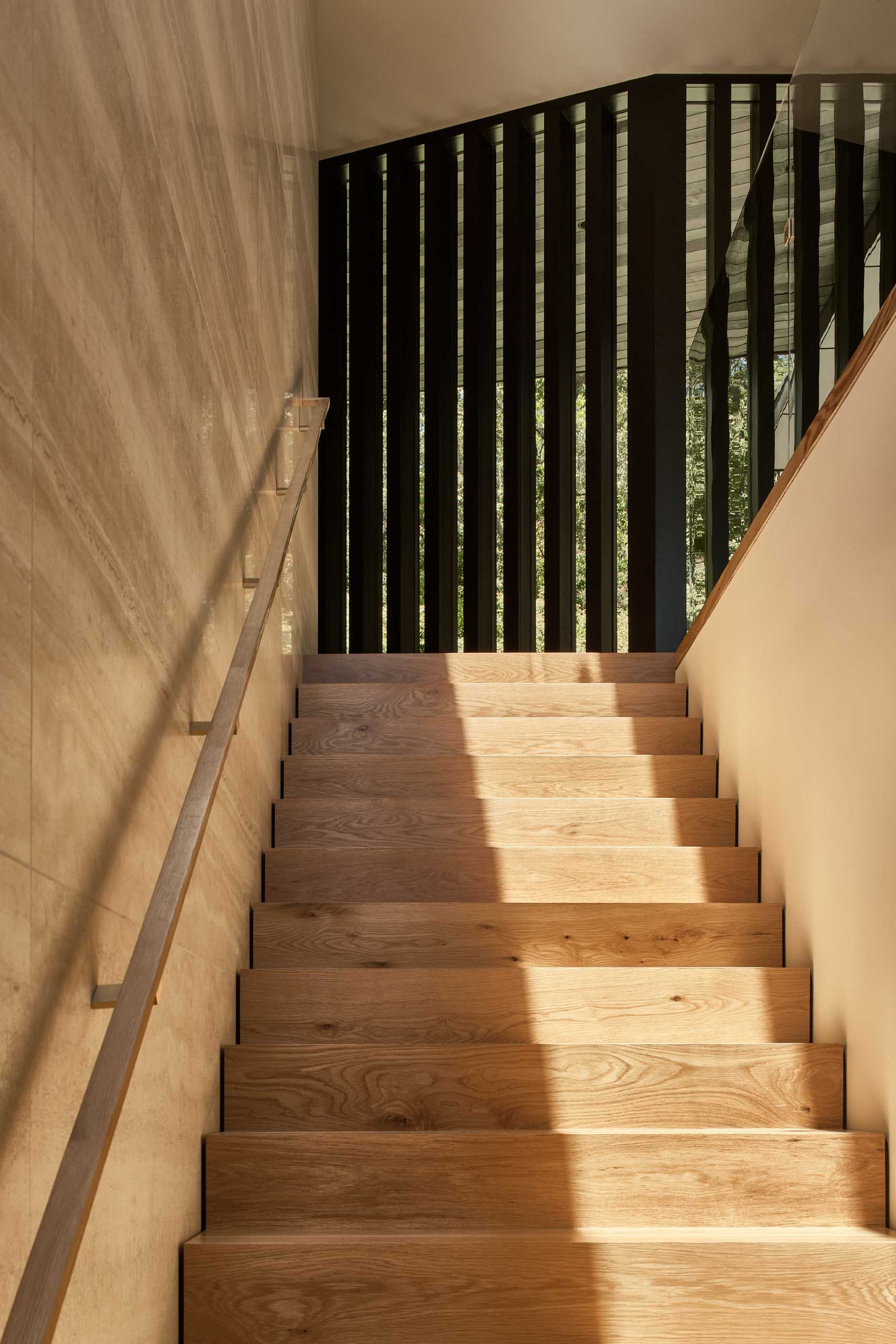 A Travertine wall runs alongside wood stairs that lead to the upper level of the ،me.