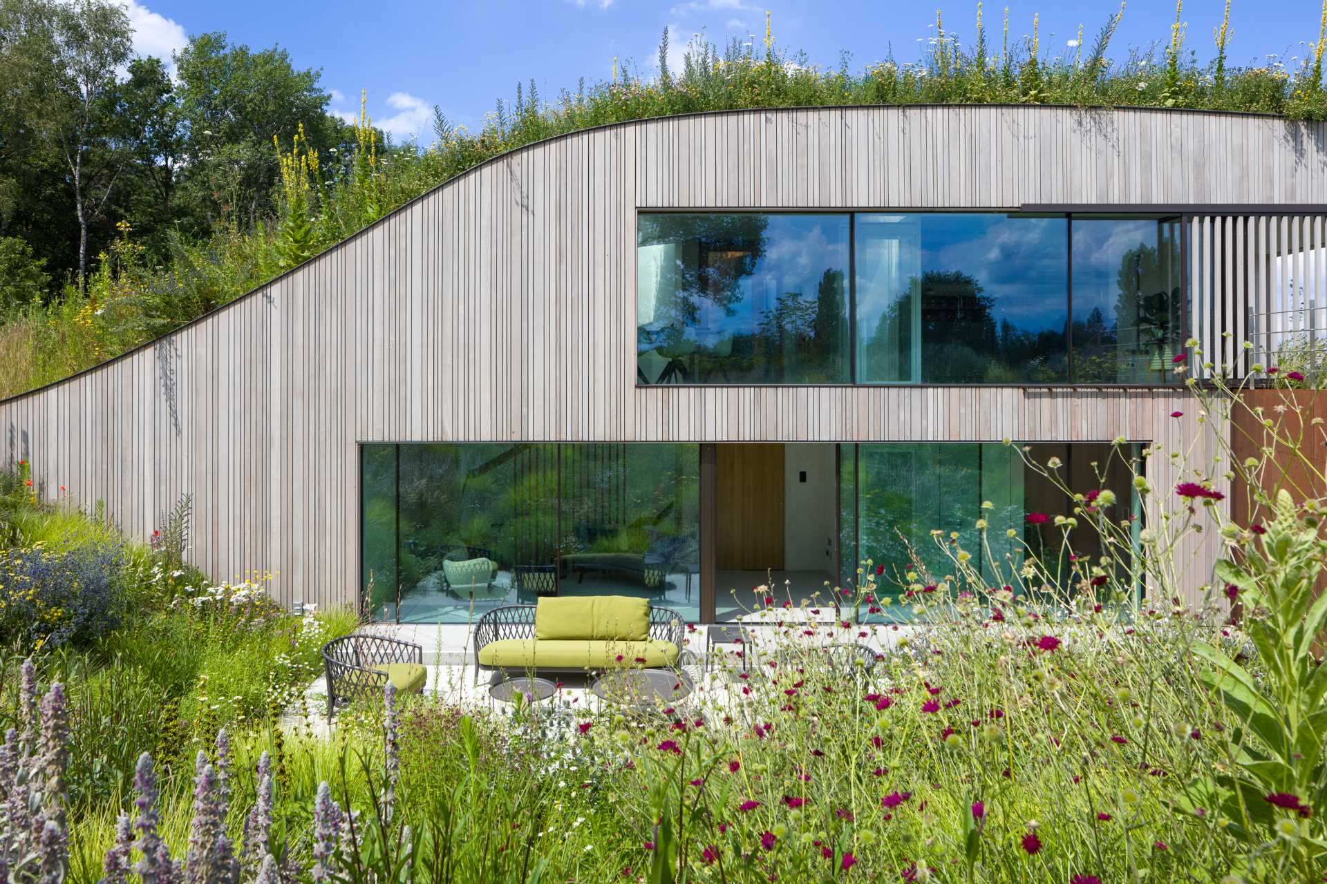 A modern house that's built into the ground and has a green roof, and multiple outdoor spaces.