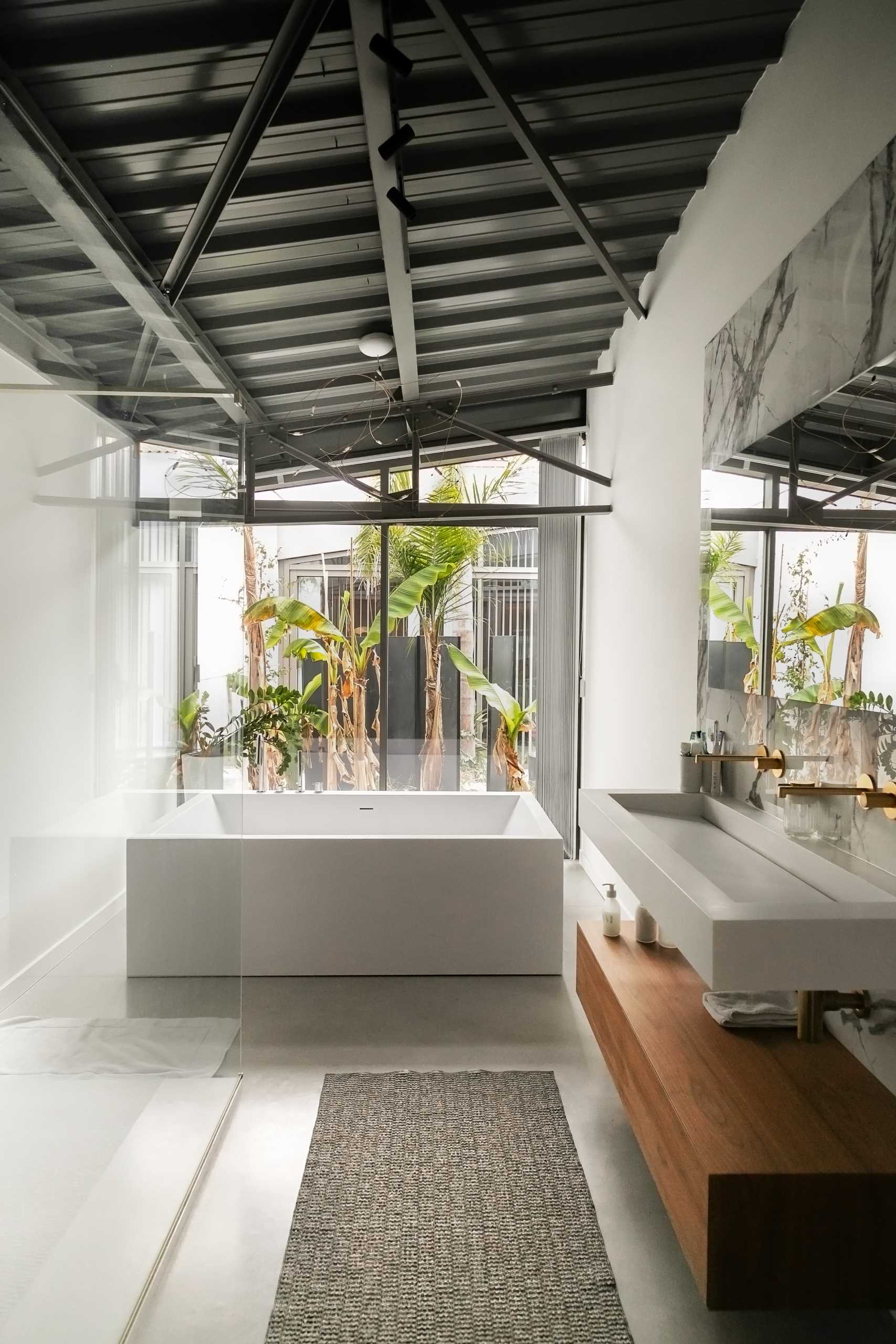 In this modern bathroom, a freestanding white bathtub is positioned in front of the windows, while a wood shelf adds a natural element.