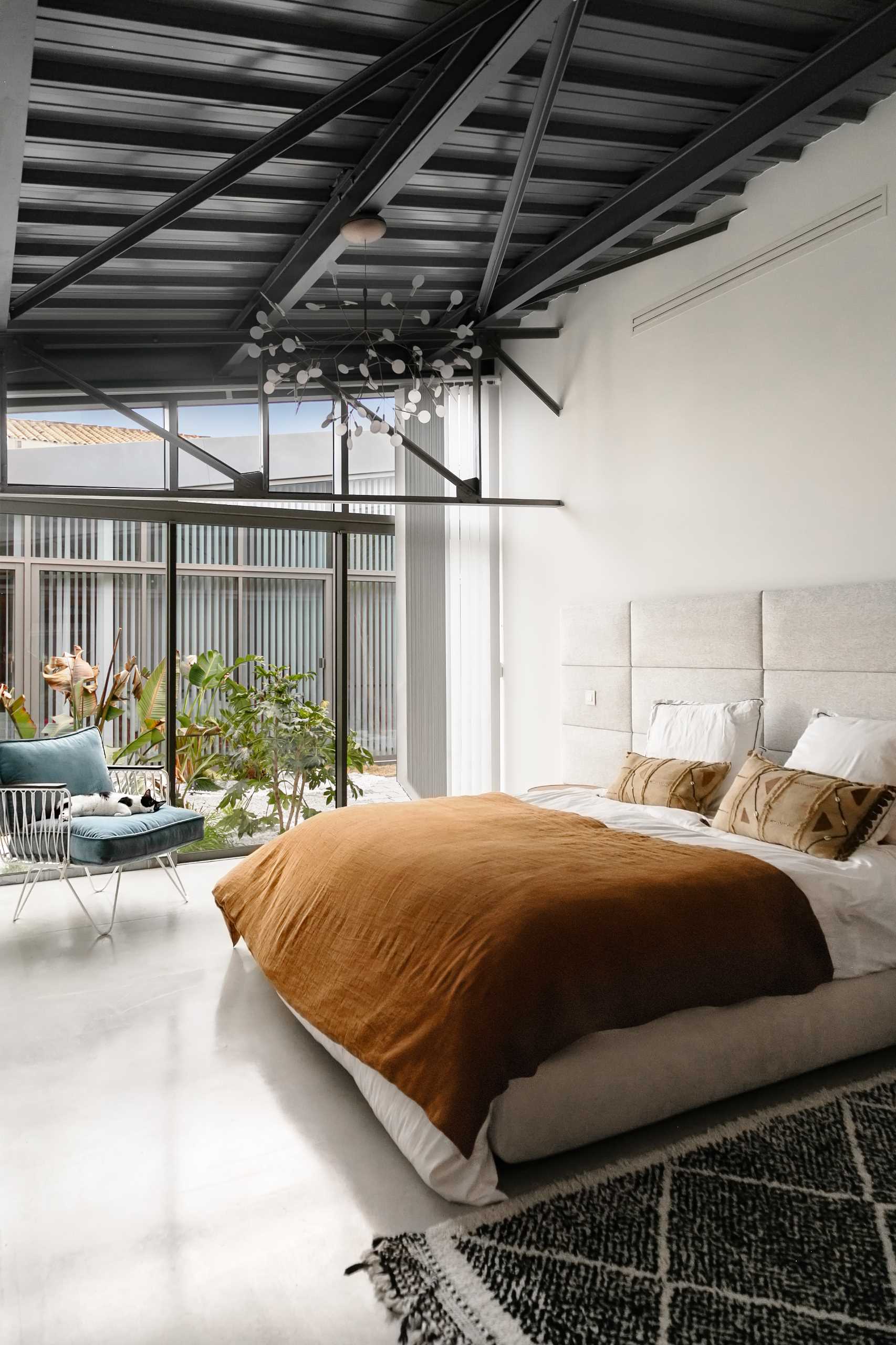 In this modern bedroom, the white walls contrast the black elements, while the windows provide a view of the plants outside.
