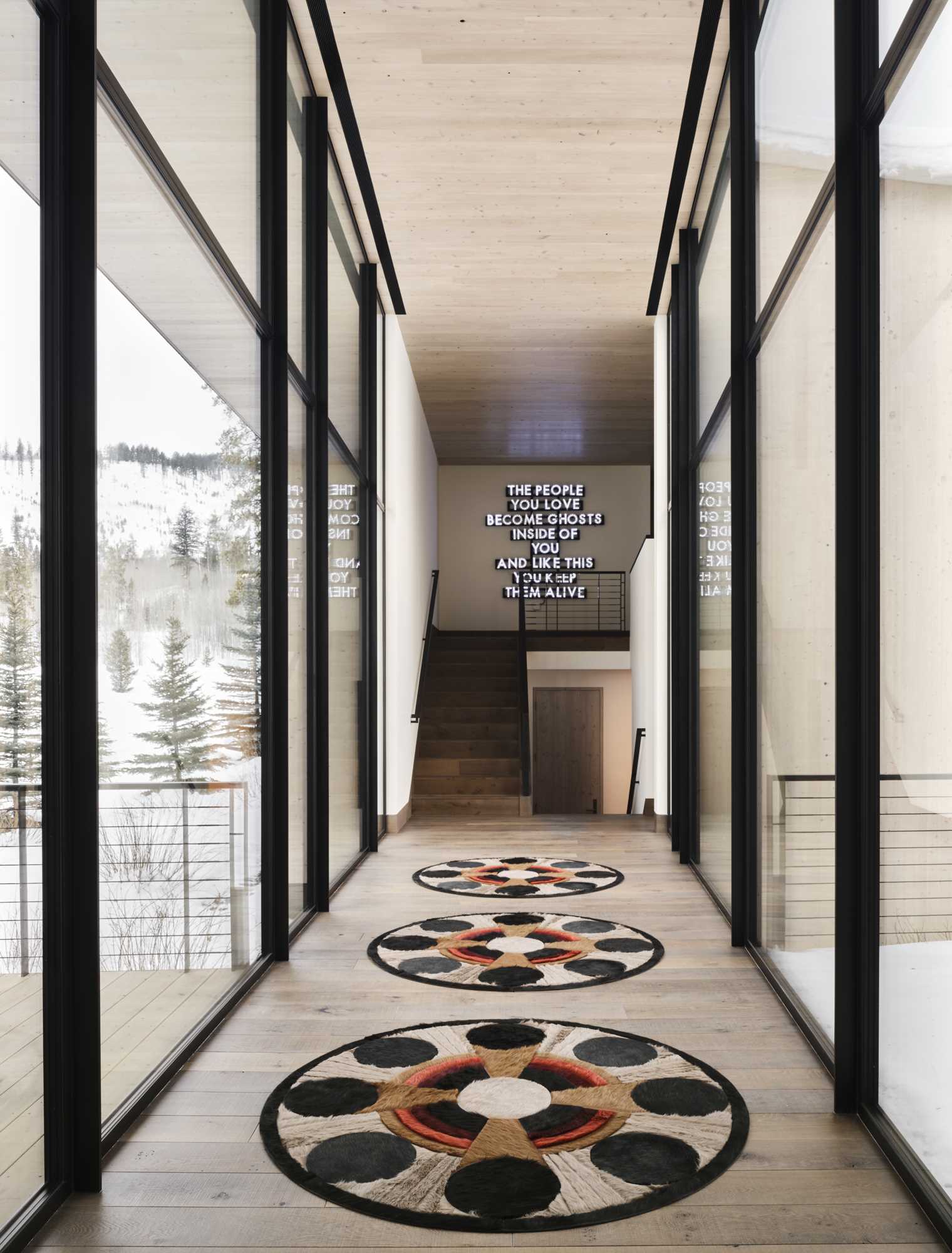 A double-height hallway with floor-to-ceiling windows with black frames s،wcase the surrounding views.