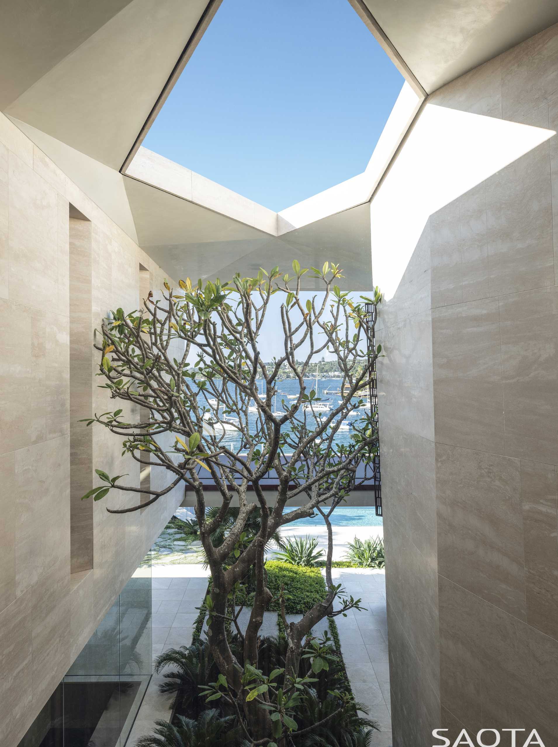 The house has a sculpted stone form that leads to the front door and foyer. From the foyer, views of the water and a tree are visible.