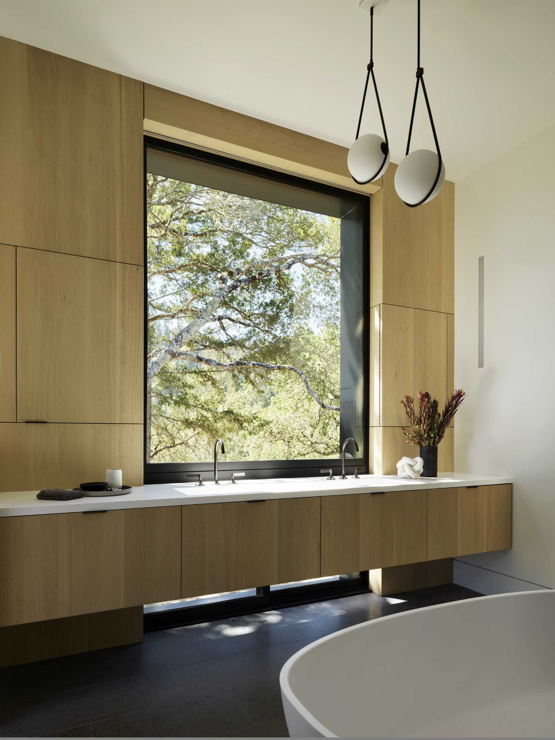 This ensuite bathroom features a wood vanity that runs the length of the wall, while a freestanding bathtub is positioned outside of the shower.