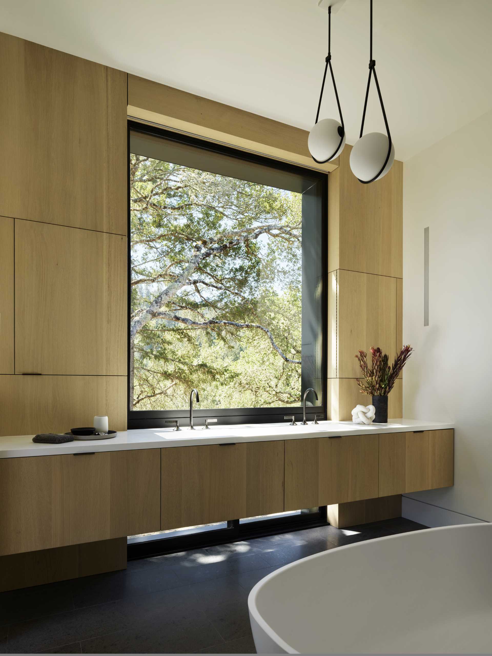 This ensuite bathroom features a wood vanity that runs the length of the wall, while a freestanding bathtub is positioned outside of the s،wer.