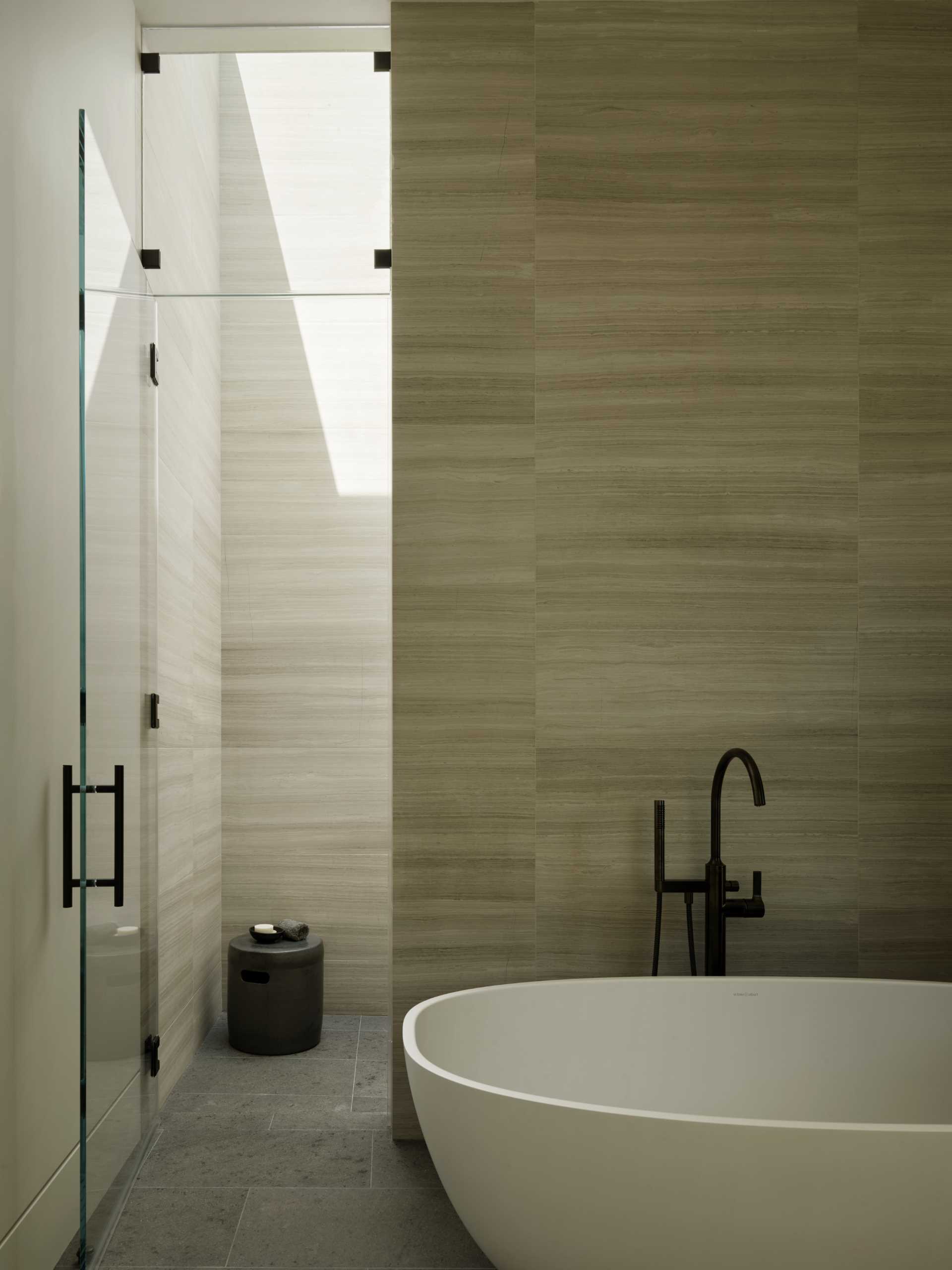 This ensuite bathroom features a wood vanity that runs the length of the wall, while a freestanding bathtub is positioned outside of the shower.