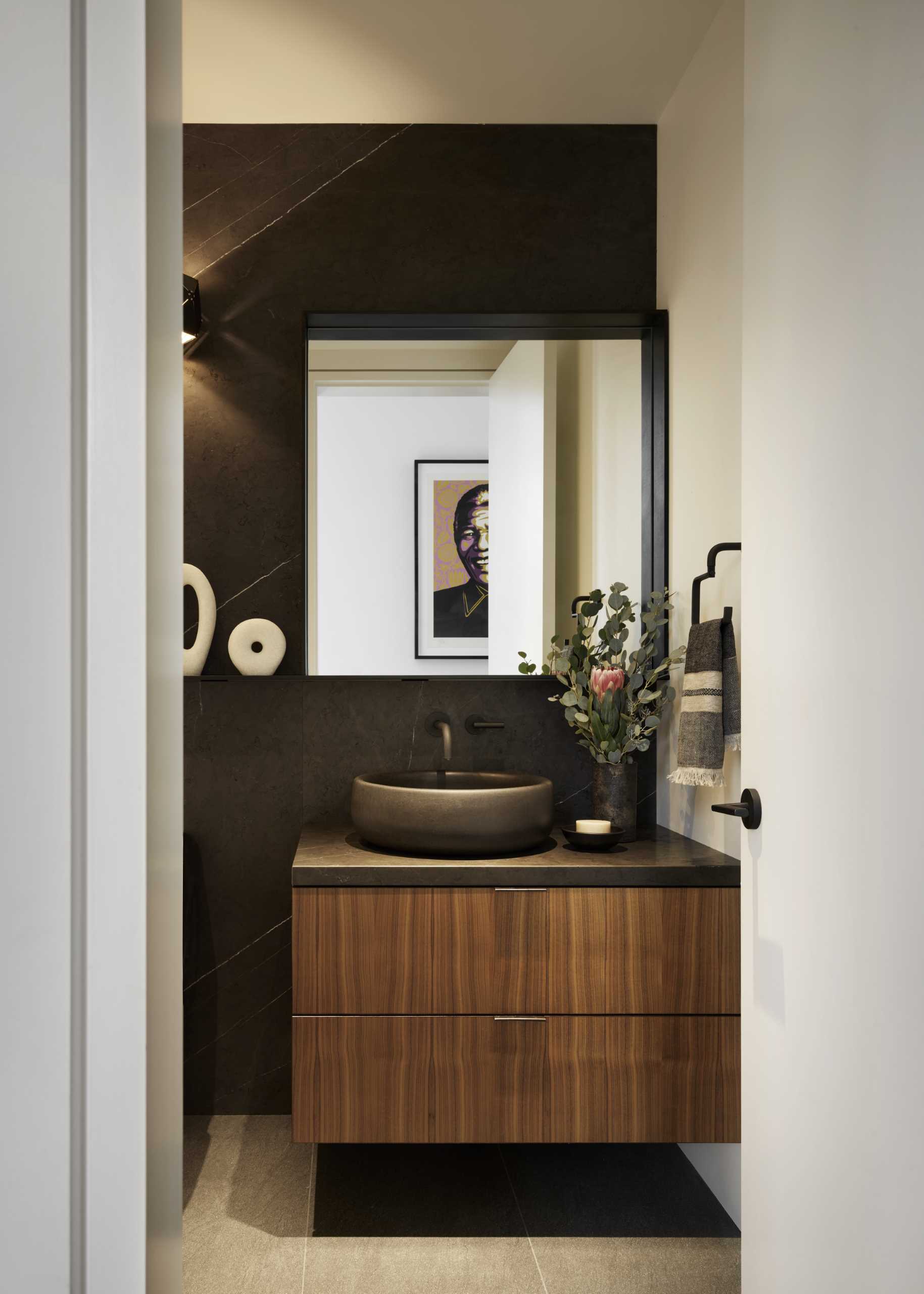 This bathroom includes a dark accent wall that matches the countertop, mirror frame, and basin.