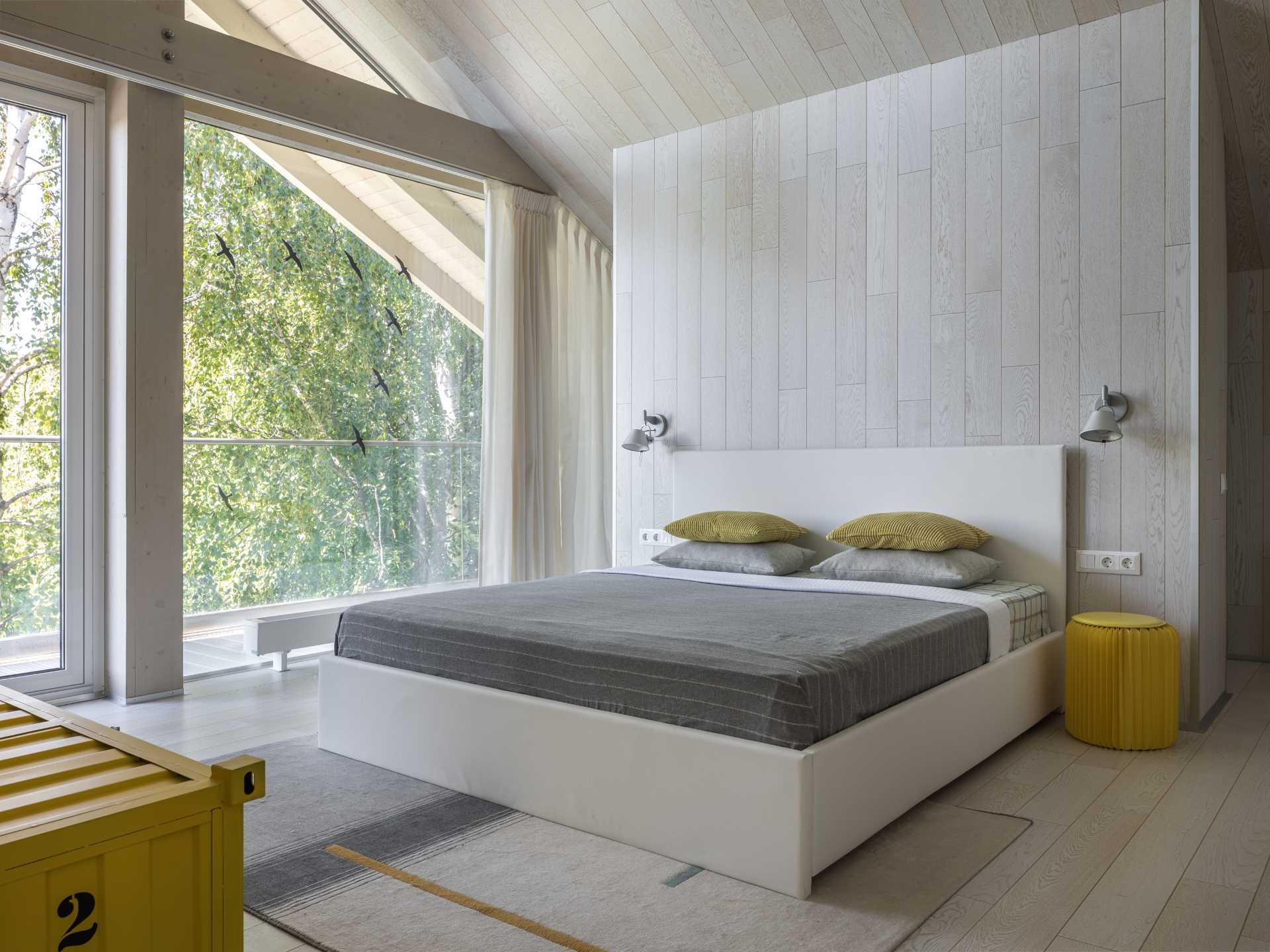 A contemporary bedroom with light wood walls and a white bed frame.