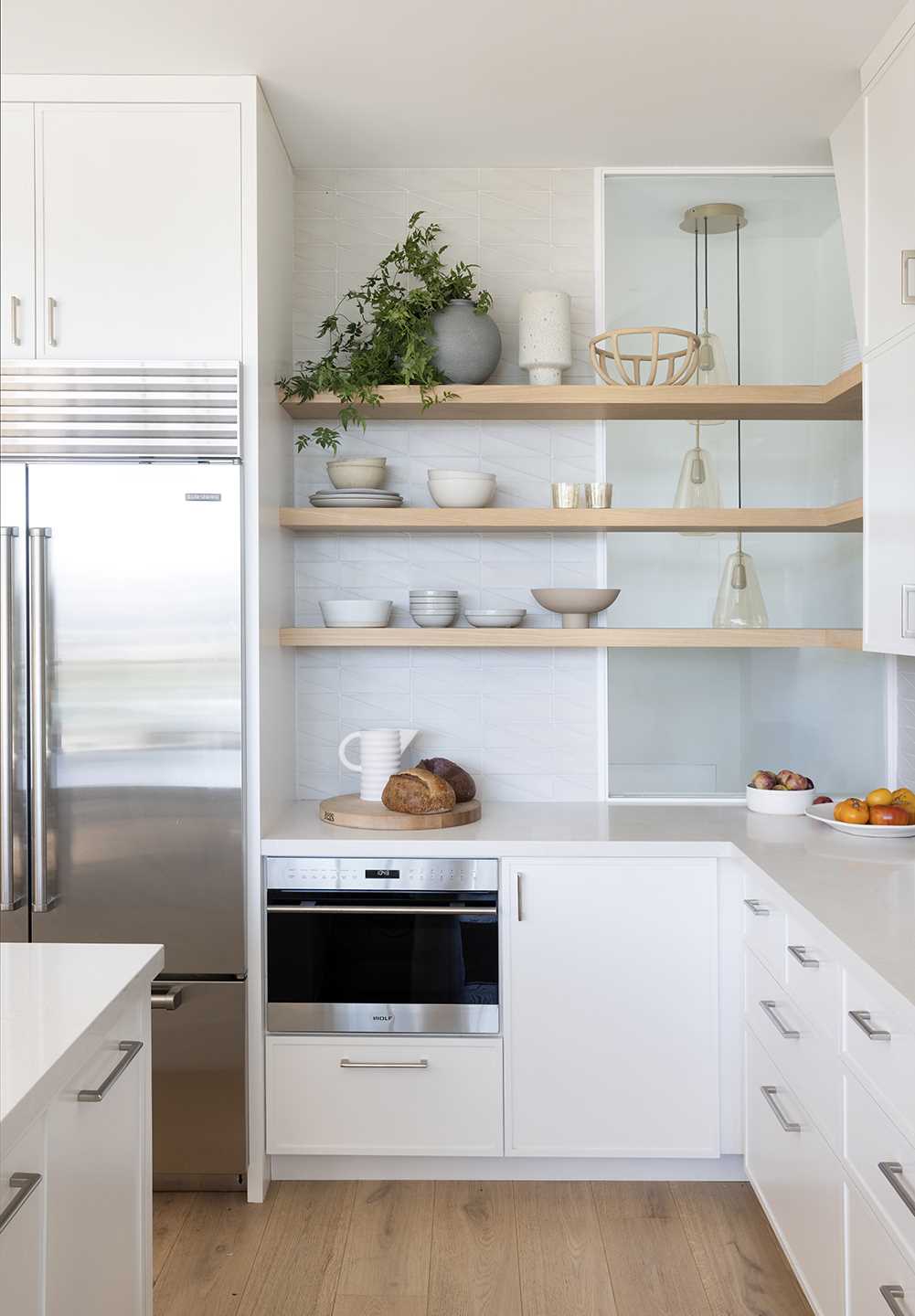 In the kitchen, white cabinets reach to the ceiling, while wood accents provide a natural touch, and a kitchen island includes a wine fridge and a place for seating. A window behind some shelves provides a glimpse of lights in the stairwell.