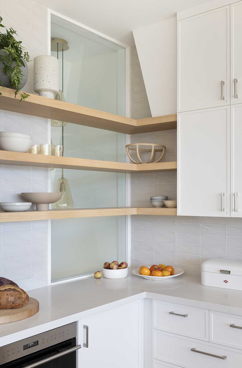 In the kitchen, white cabinets reach to the ceiling, while wood accents provide a natural touch, and a kitchen island includes a wine fridge and a place for seating. A window behind some shelves provides a glimpse of lights in the stairwell.