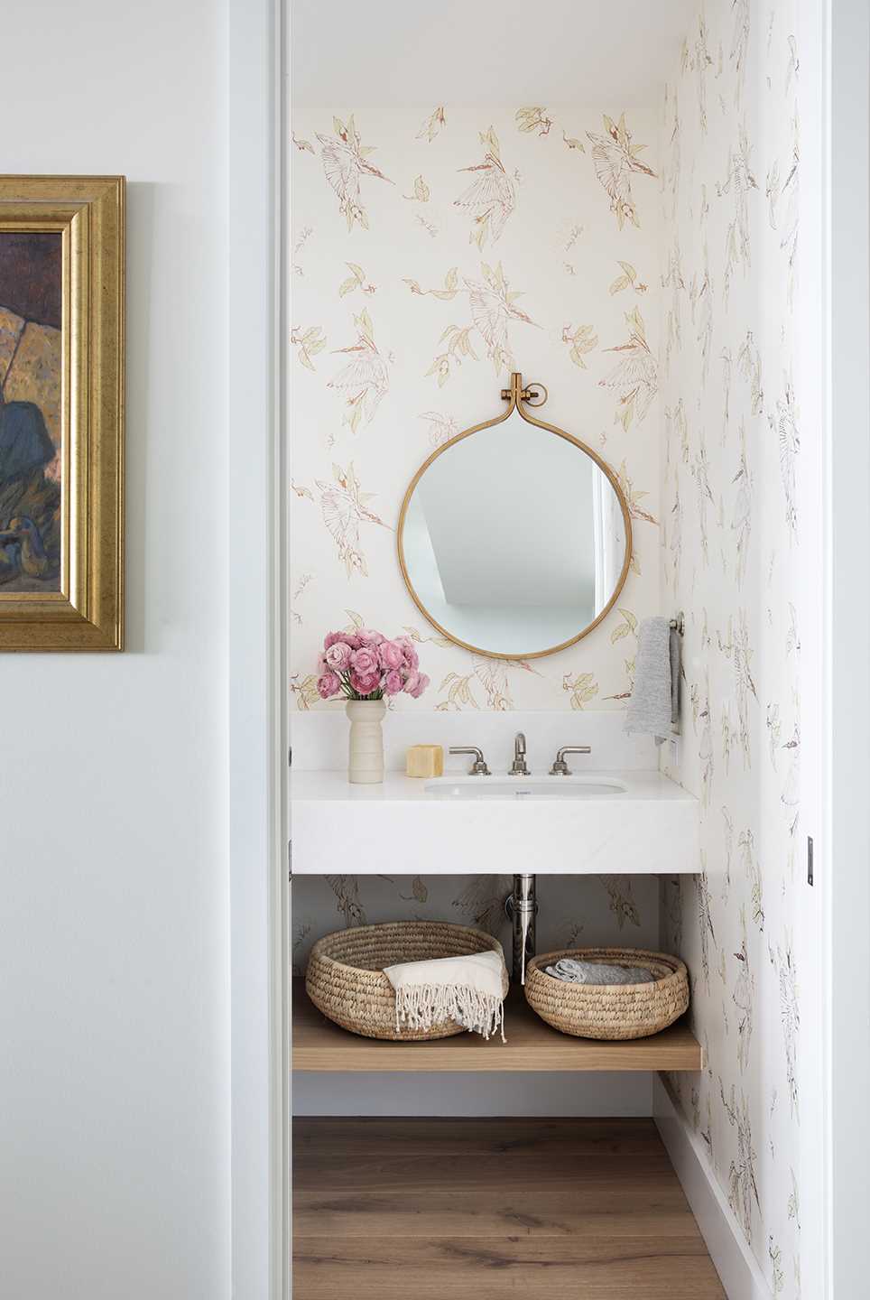 A modern powder room with a delicate wallpaper and round mirror.