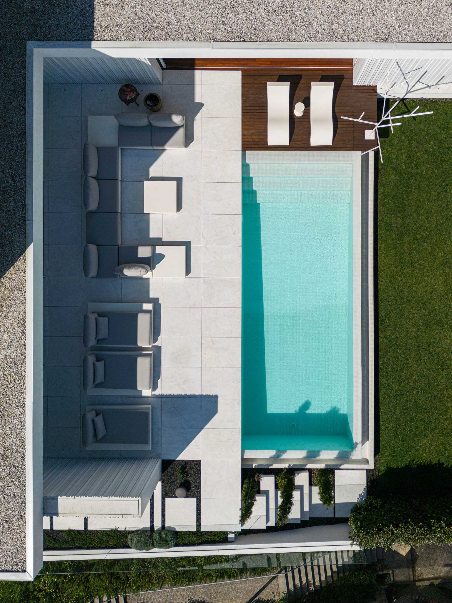 A modern home features an exterior of white concrete with textured accent walls, and a swimming pool with expansive patio.