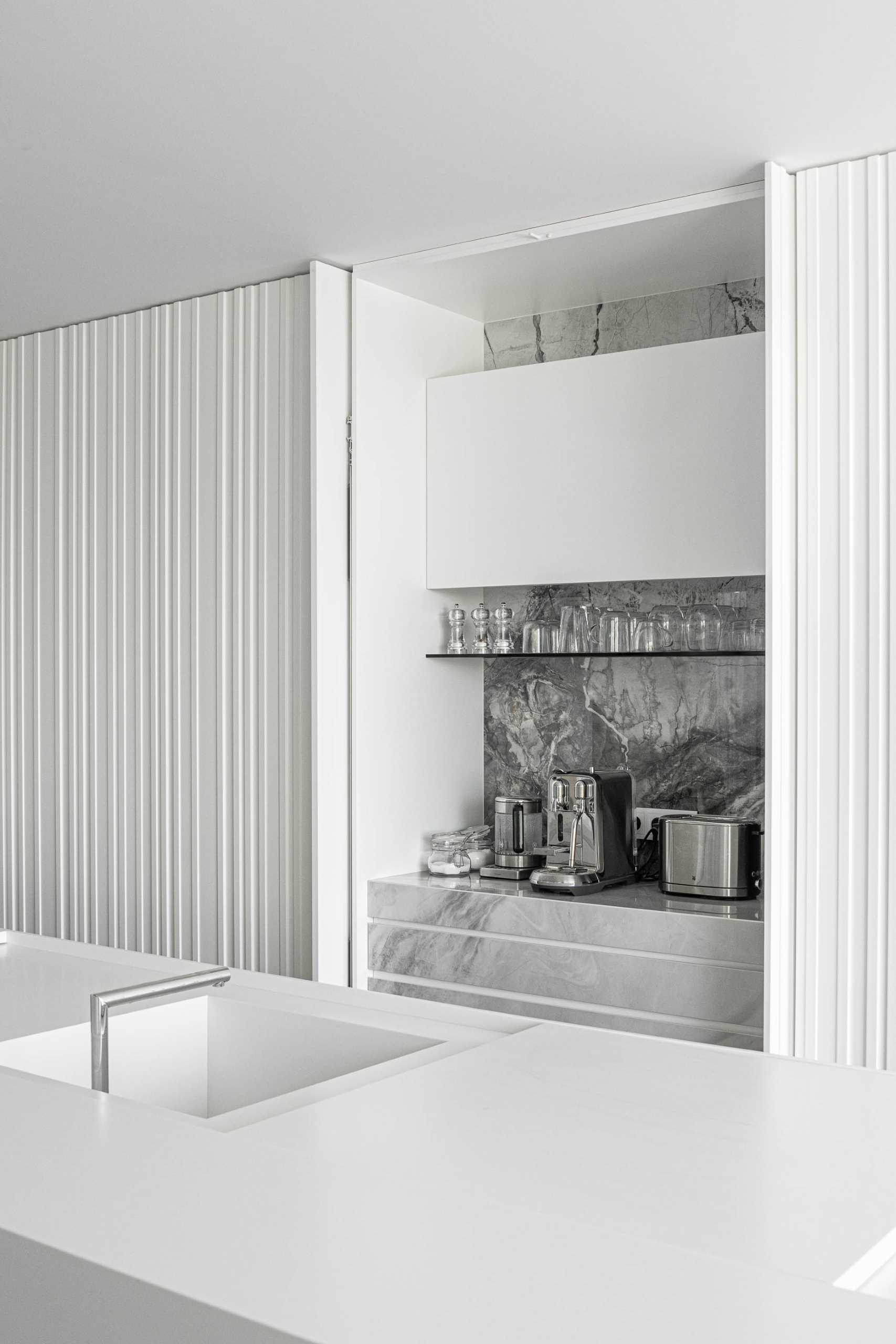 In this modern white kitchen, the textured wall hides the kitchen cabinets, while a sculptural light adds an artistic moment.