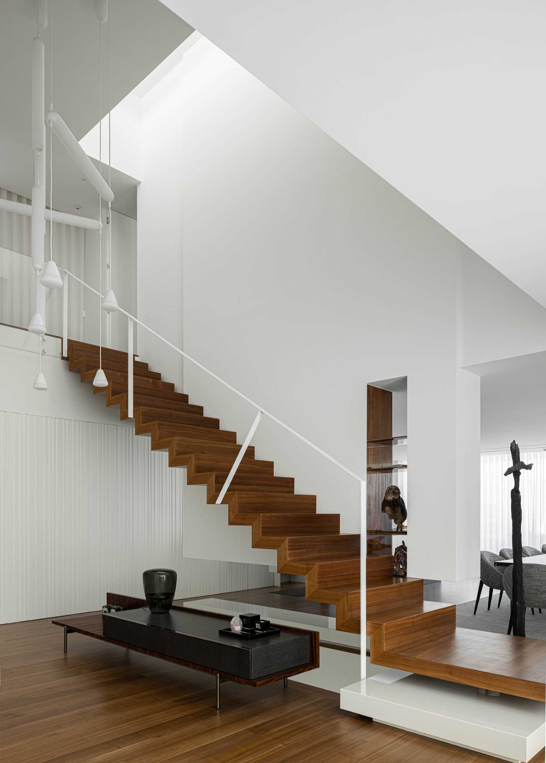 Wood stairs with white handrails connect the social areas of the home with the more private spaces upstairs.