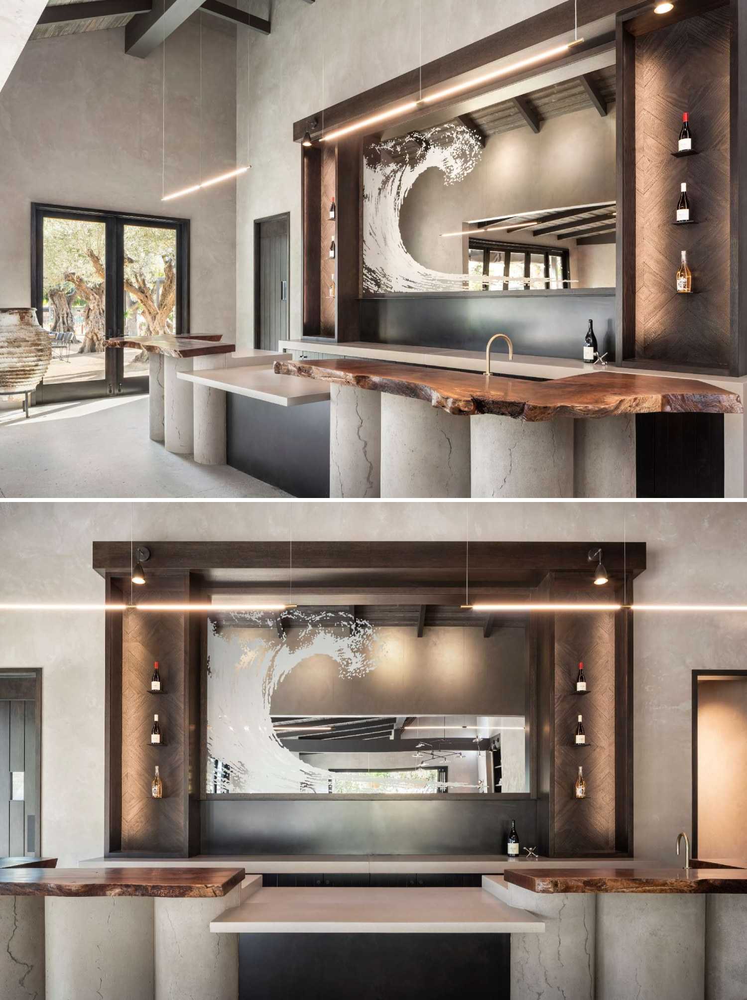 In a wine tasting room, a live-edge wood bar rests on concrete pillars, with a custom bronzed mirror catching the light behind it.
