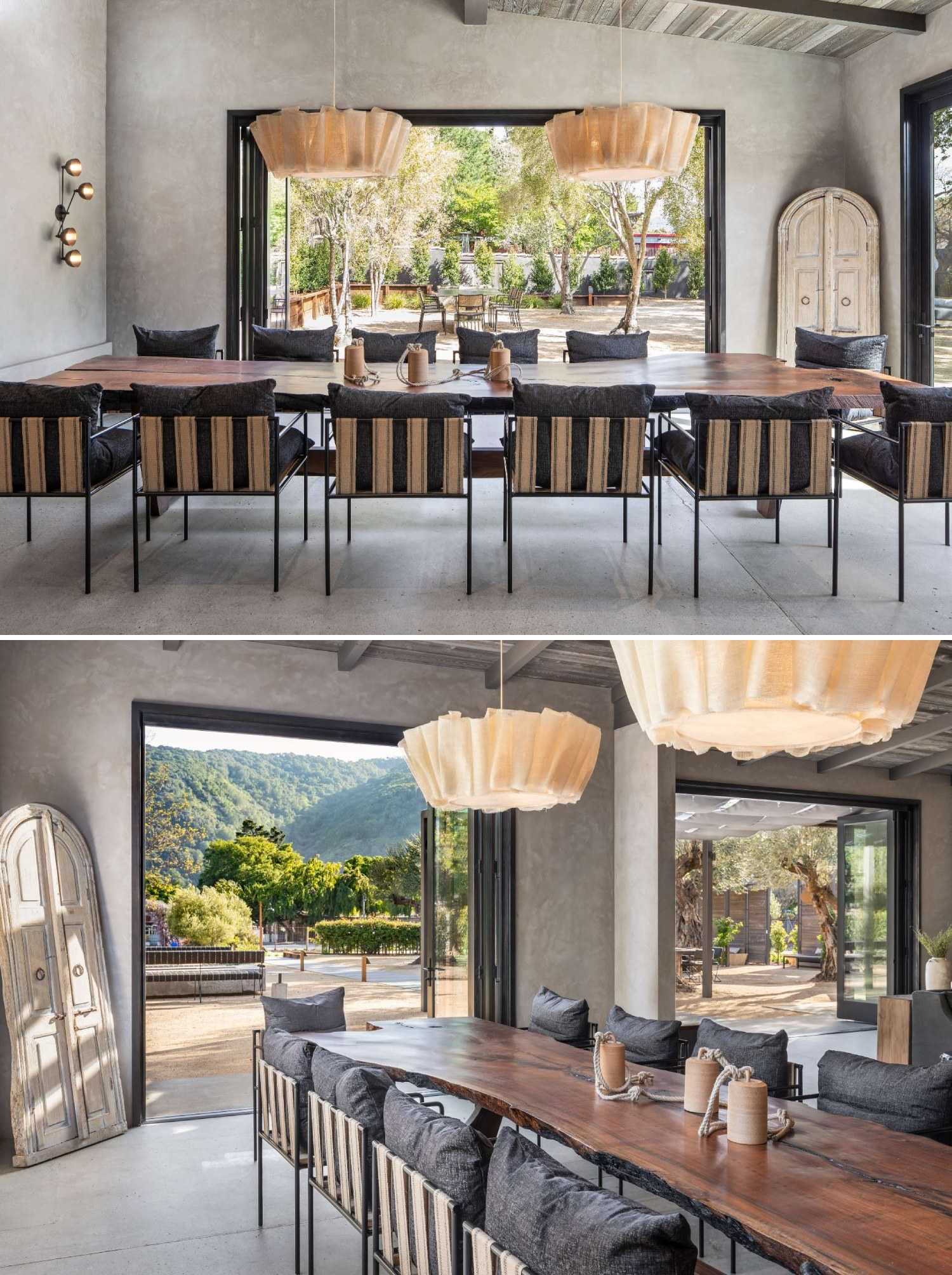 In a wine tasting room, a long communal live-edge dining table sits beneath pendant lights from Pinch, framed by views of the garden beyond.