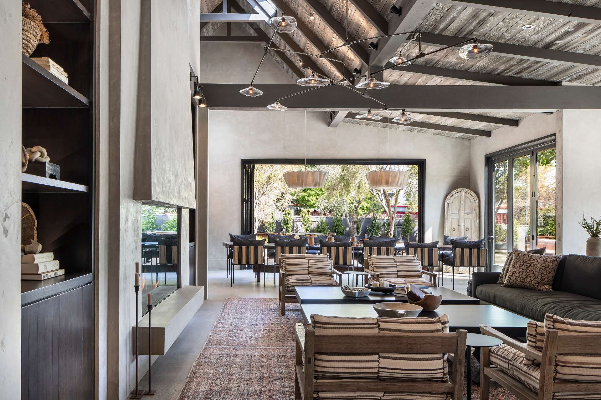 Inside this wine tasting room, the palette leans natural and textural. Plastered walls meet polished concrete floors, and a dark-stained wood ceiling adds warmth overhead. Cabinets made from Shou Sugi ban (charred wood) bring depth without shouting for attention. A central fireplace marks the heart of the space, surrounded by relaxed lounge seating. Nothing feels overdesigned, yet everything has presence.