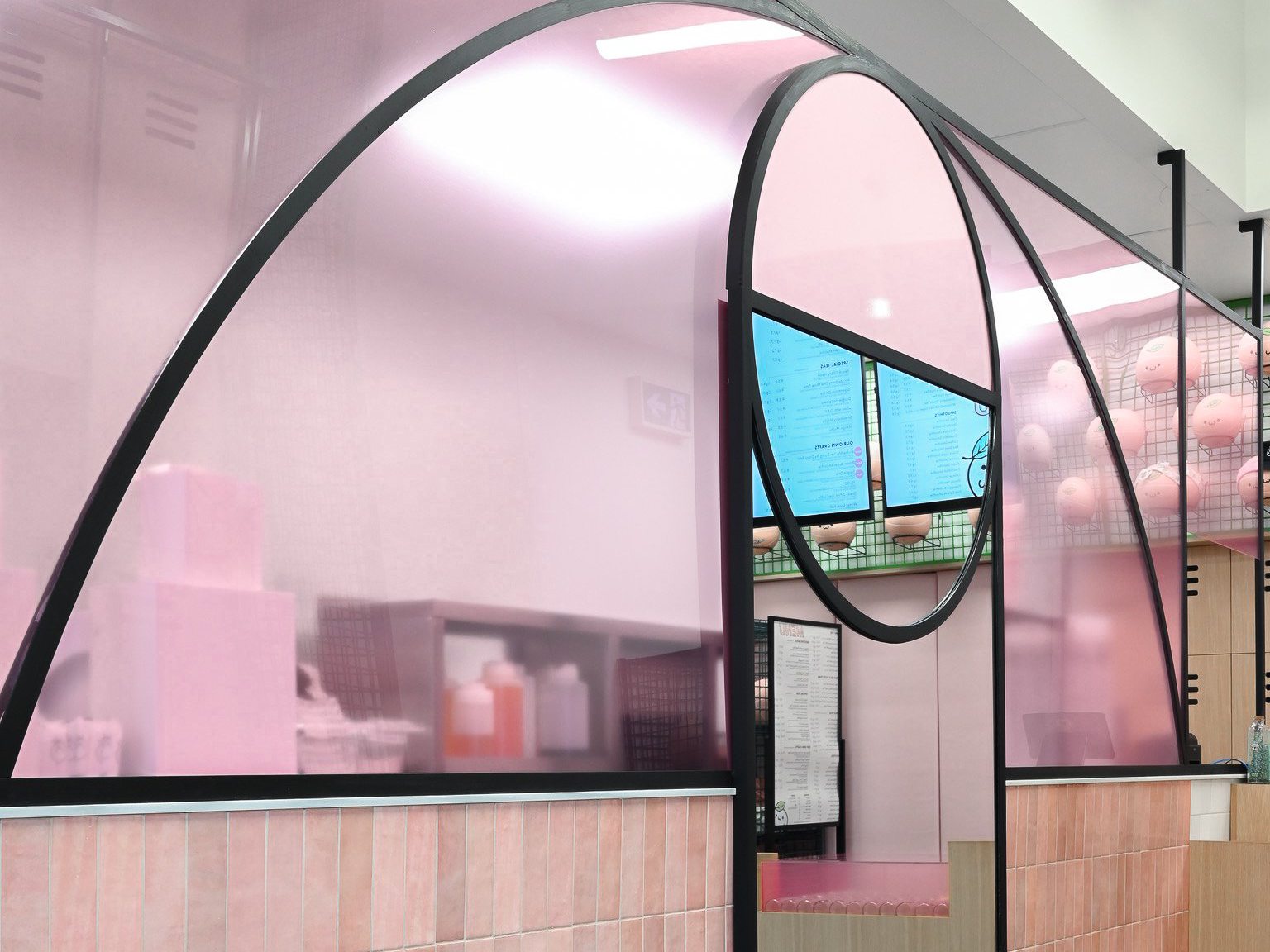 A playful take on bubble tea design, this shop features pink plexiglass panels shaped like basketball court lines and a peek-through window that frames the menu. The curved details and soft color palette add charm while giving a nod to sporty, kawaii-inspired interiors.