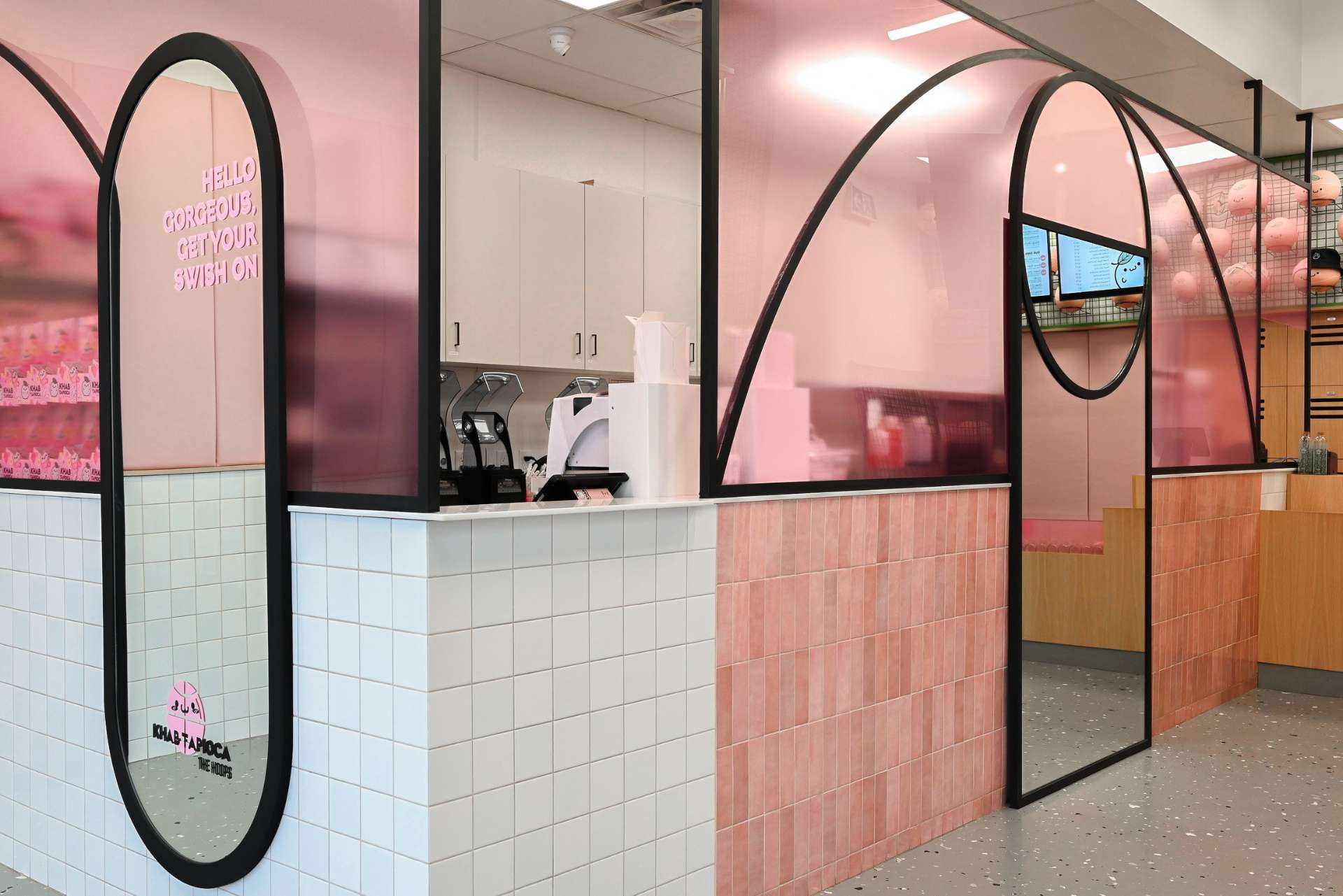 This bubble tea shop blends bold design with playful charm using curved black frames that mimic basketball court lines, soft pink and white tile, and a full-length mirror that adds depth and personality. A vibrant mix of sport and sweetness brought to life in a compact, curated space.
