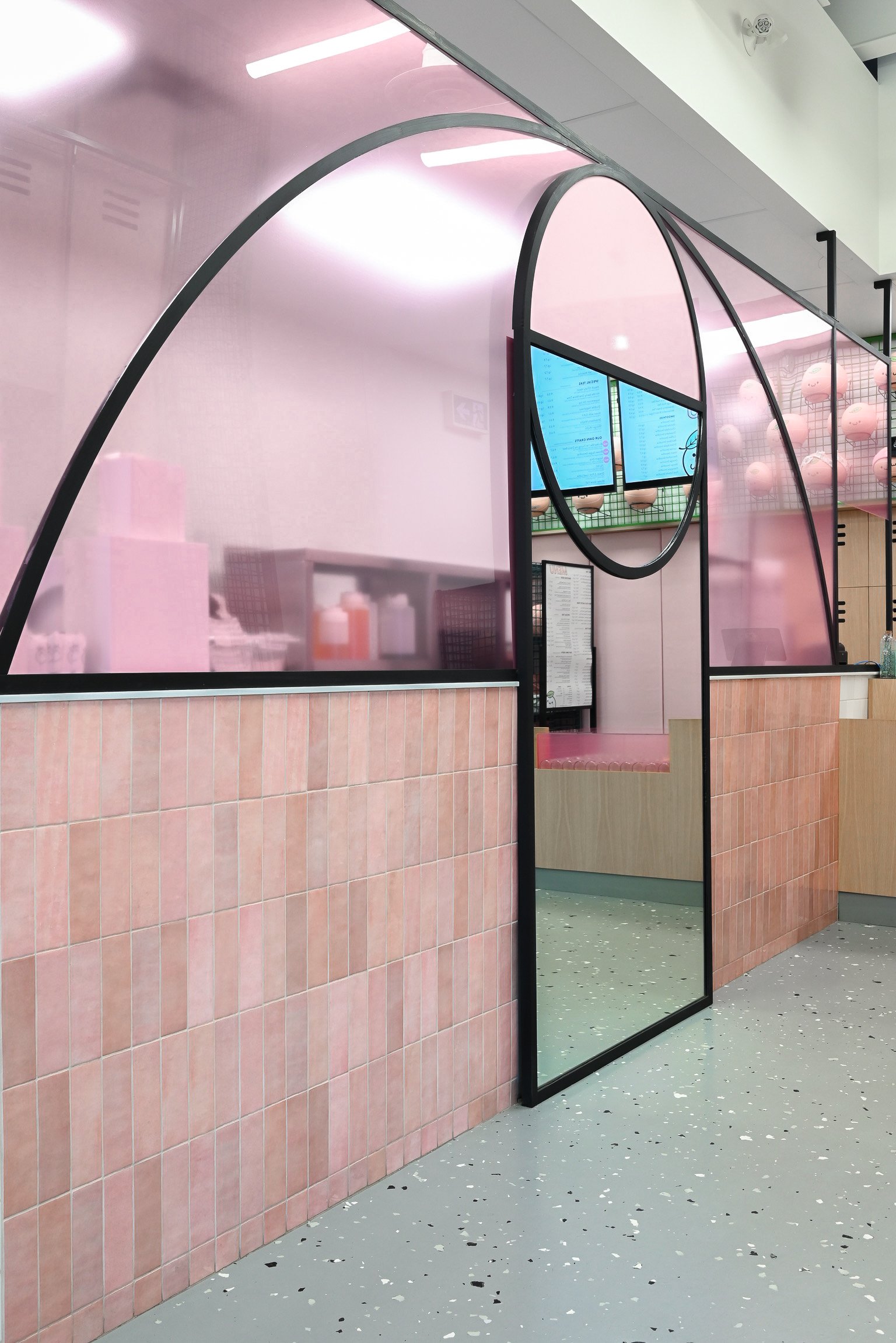This bubble tea shop blends bold design with playful charm using curved black frames that mimic basketball court lines, soft pink tile, and a full-length mirror that adds depth and personality. A vibrant mix of sport and sweetness brought to life in a compact, curated space.