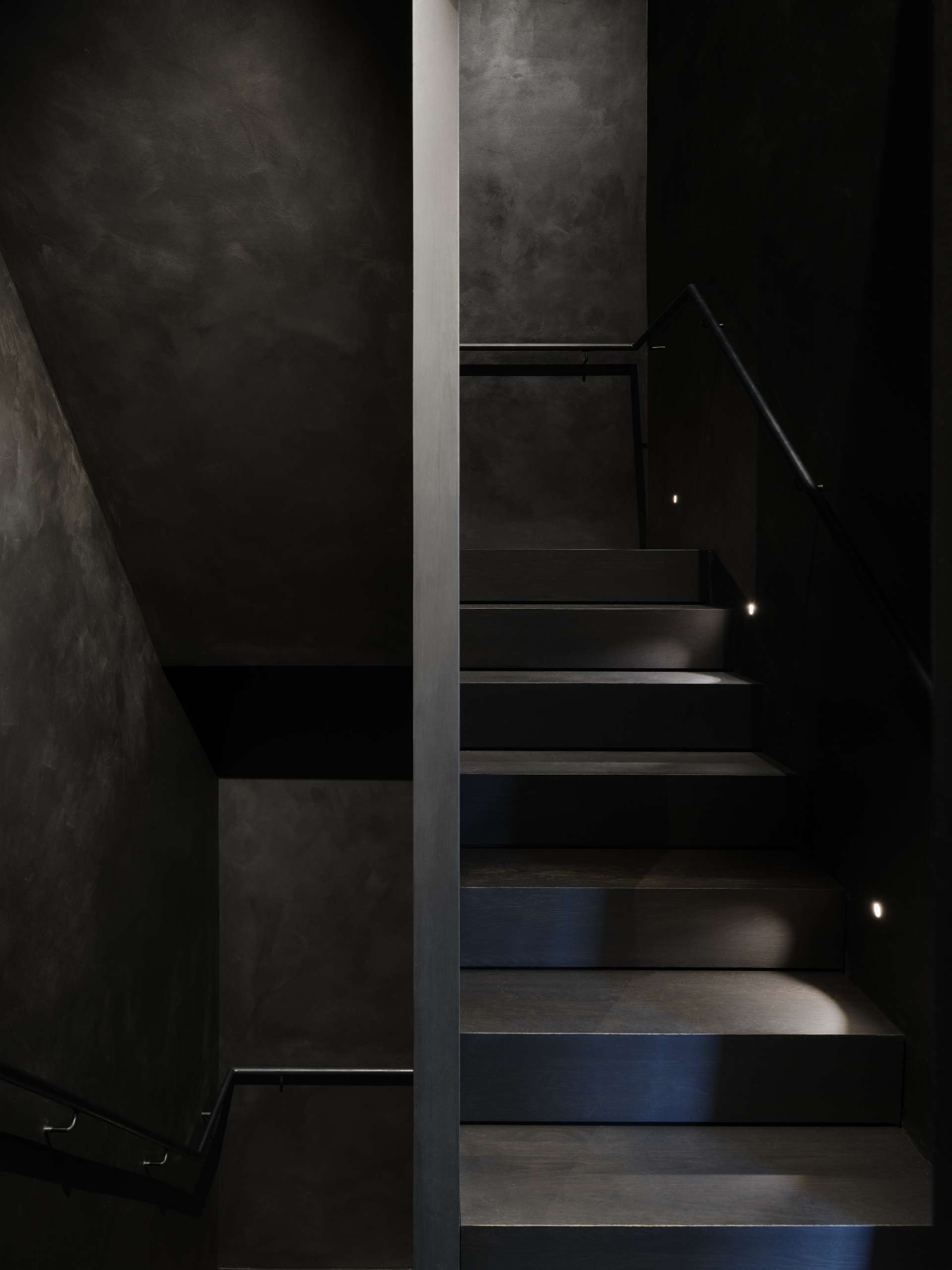 At the center of the home, the staircase connects the floors with quiet elegance and a dark material palette.