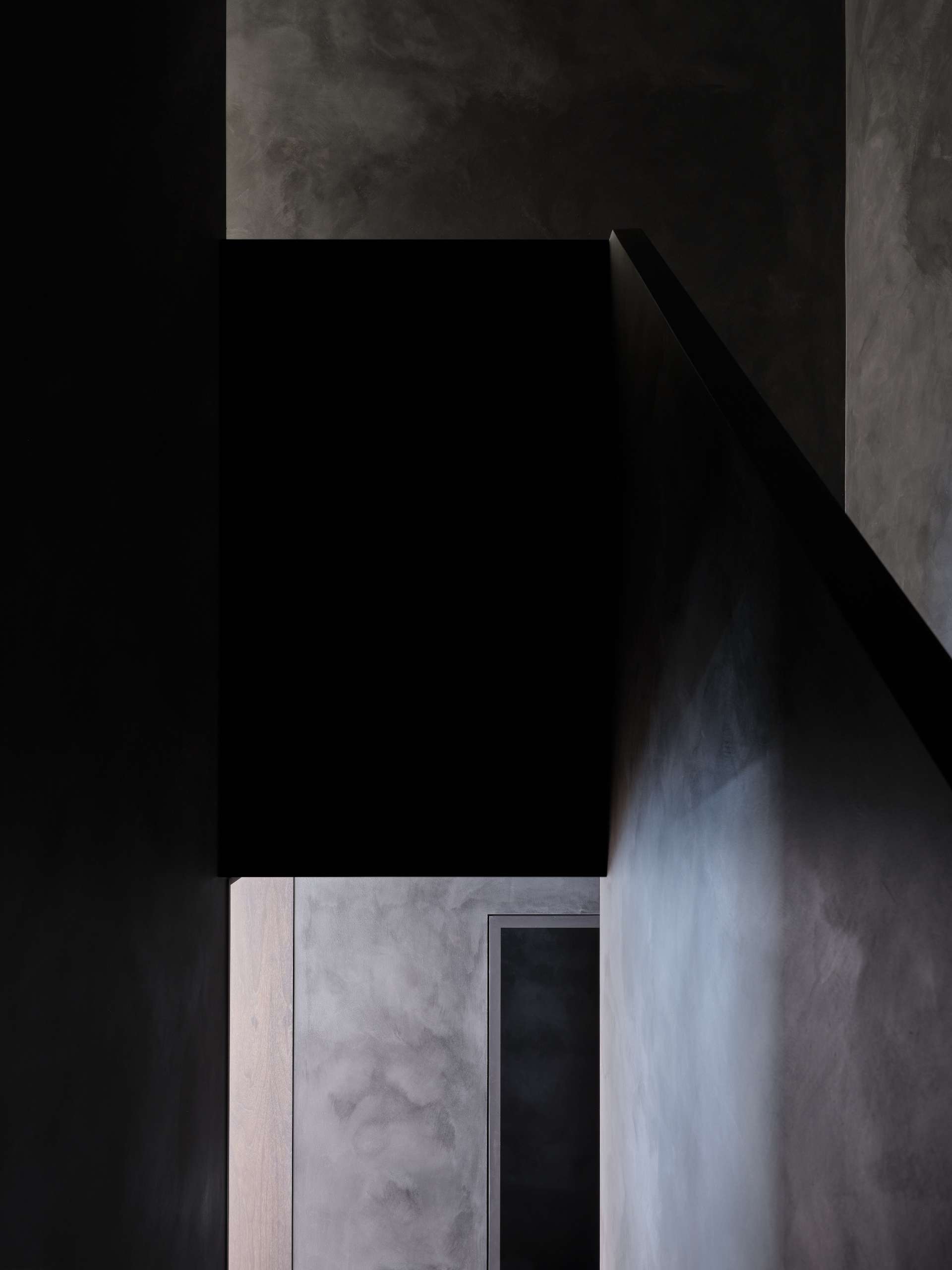 At the center of the home, the staircase connects the floors with quiet elegance and a dark material palette.