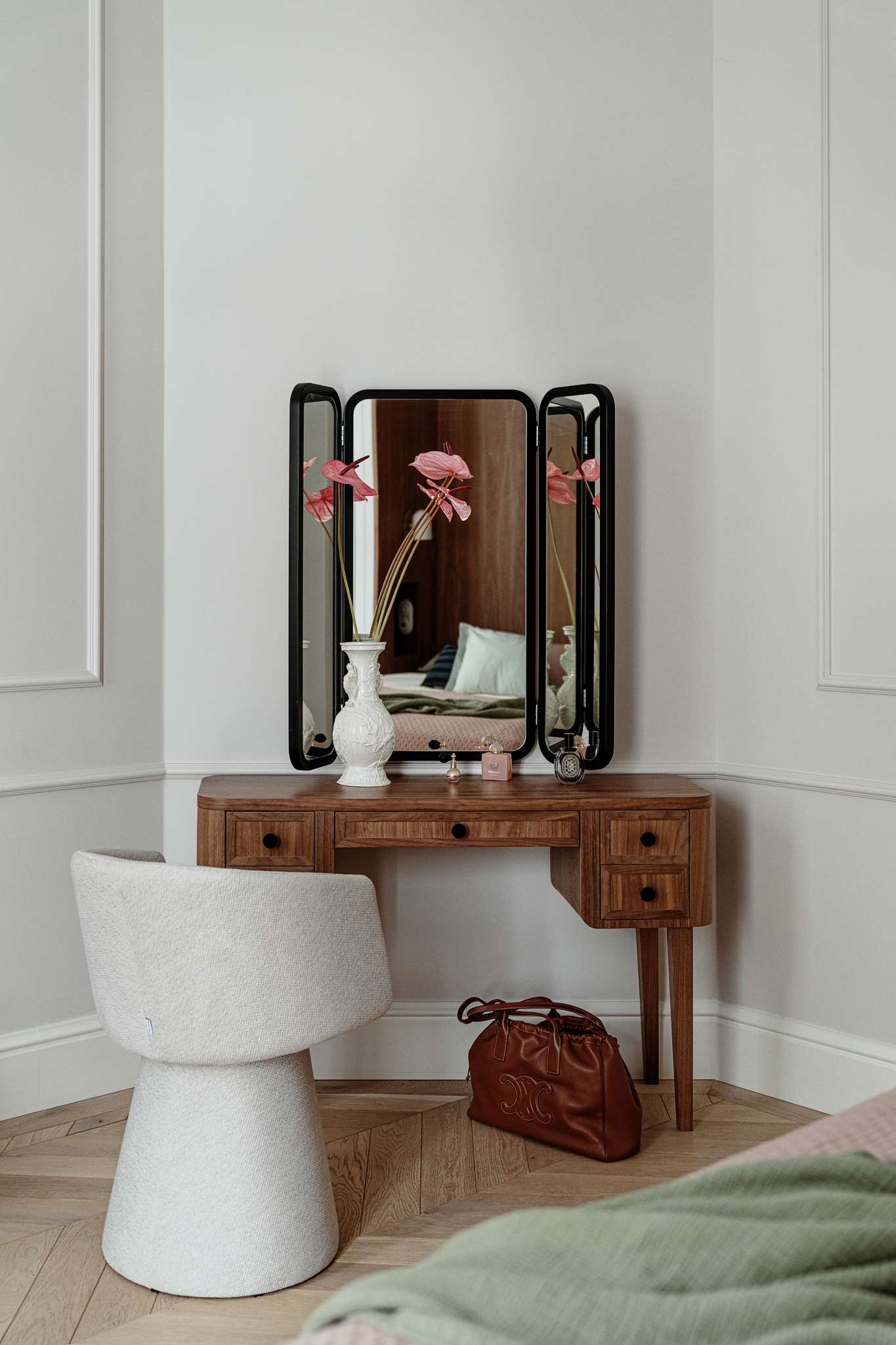 In the corner of this bedroom, a wood vanity with a three-panel mirror and vintage styling creates a personal, graceful moment that ties the room together.