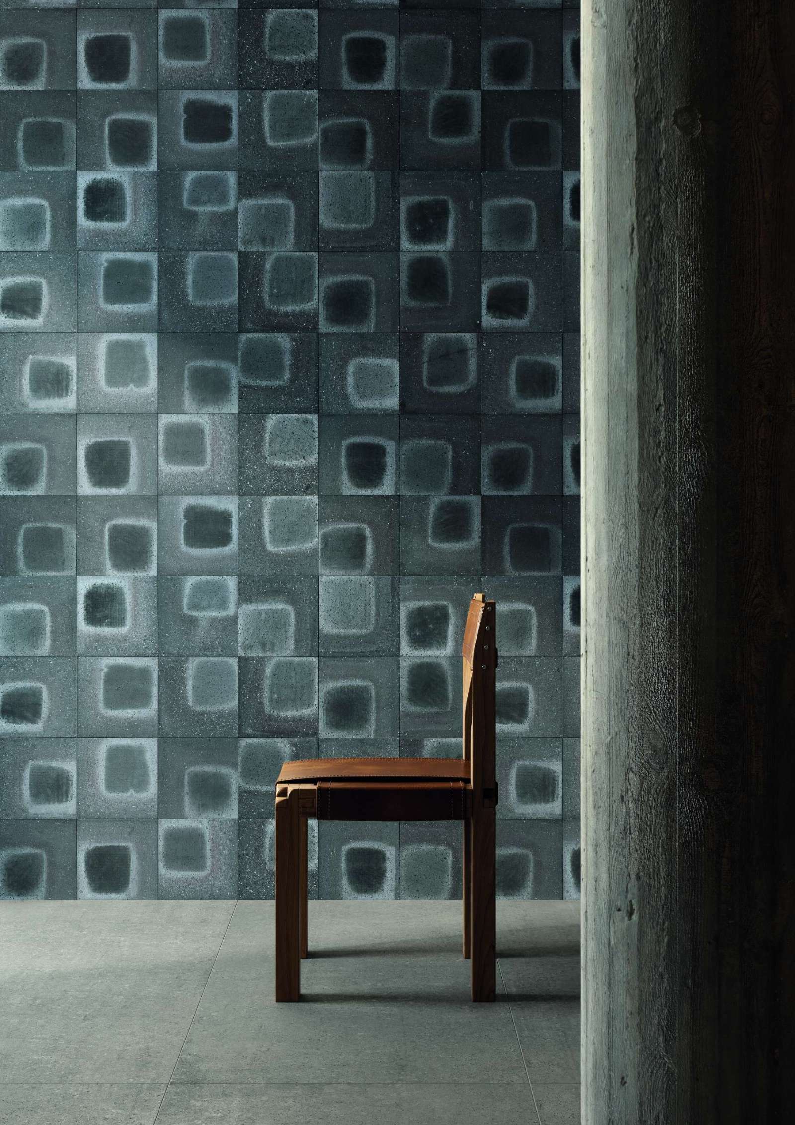 This geometric wall tile brings depth and movement to any space with its hand-painted square pattern and moody blue-gray tones. A minimalist chair and raw concrete add to the gallery-like atmosphere.