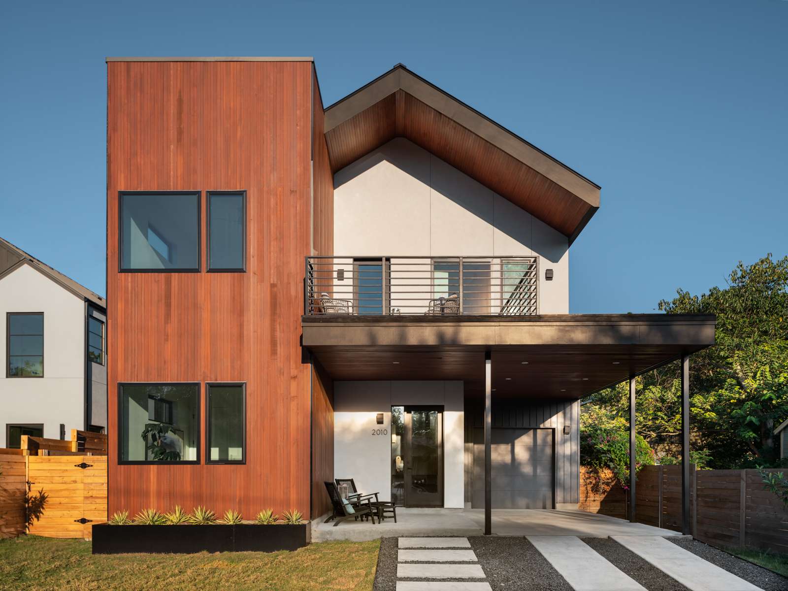 The front facade of the Oxford Avenue home blends clean geometry with inviting material contrast. A vertical volume clad in rich natural wood softens the modern silhouette and brings warmth to the overall composition. In contrast, smooth light-toned stucco defines the main body of the home, offering a crisp backdrop that accentuates the deep overhangs and angular roofline.