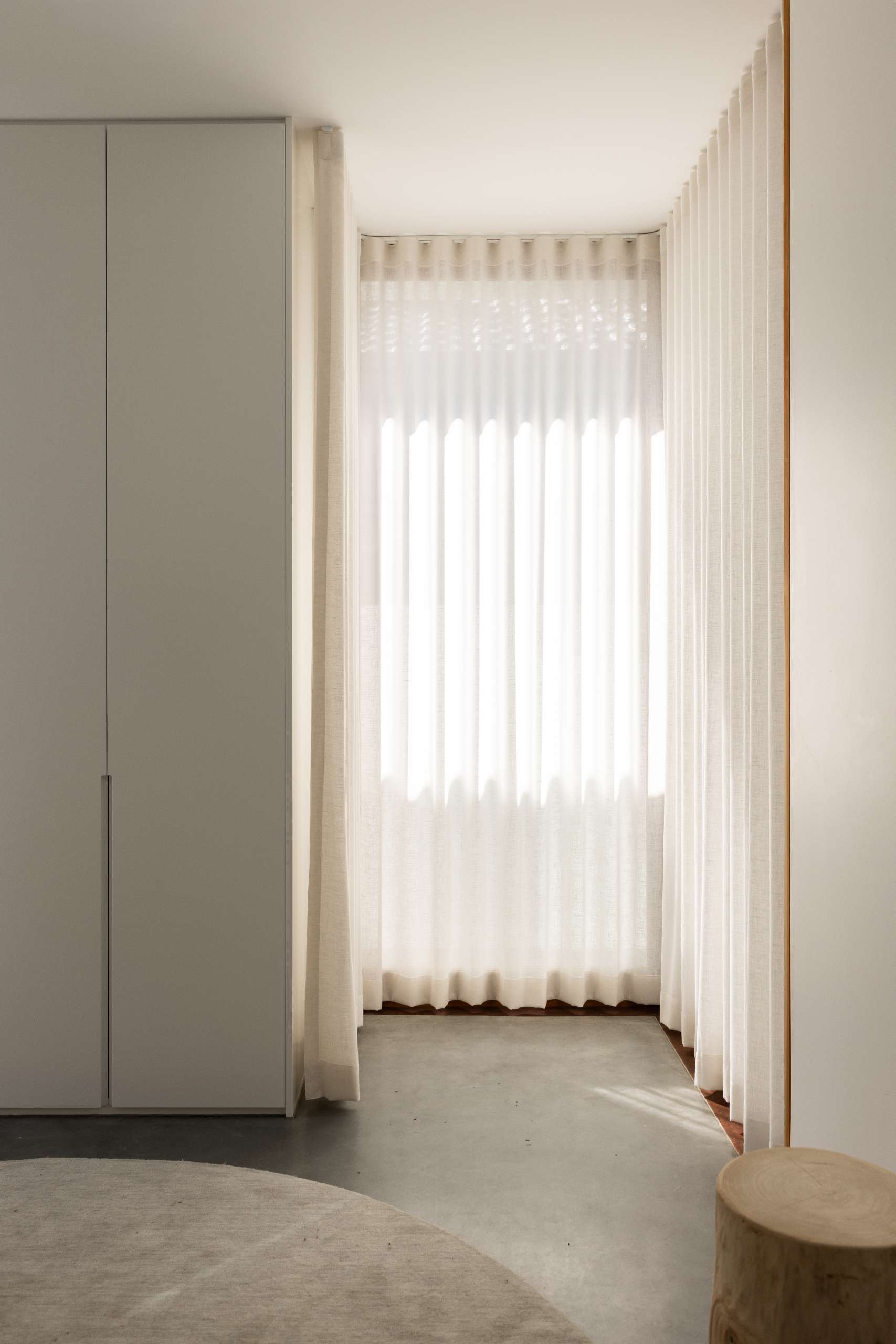 Corner sliding doors open this minimalist playroom to a private deck, while sheer curtains and built-in cabinetry keep the space bright and clutter-free. A round rug softens the polished concrete floor for a cozy play area.