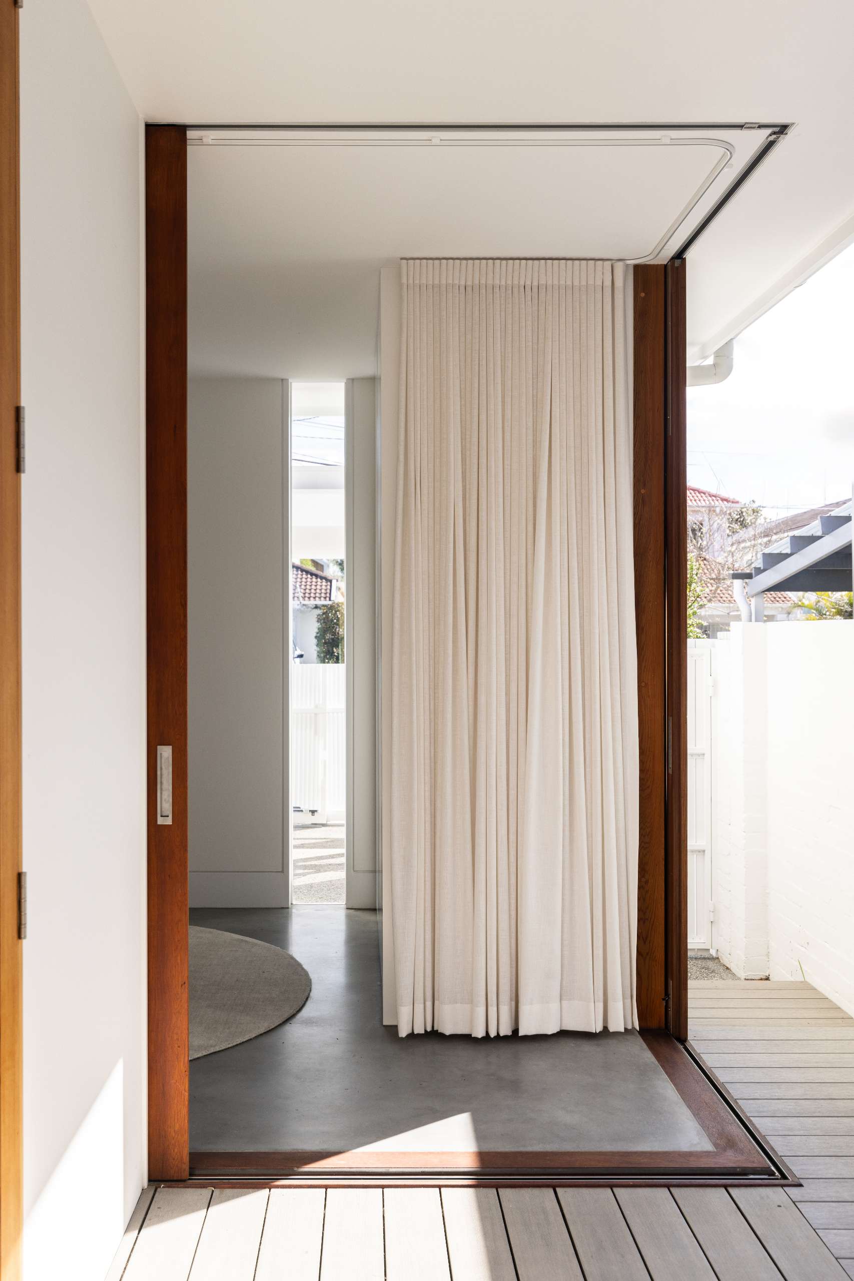 Corner sliding doors open this minimalist playroom to a private deck, while sheer curtains and built-in cabinetry keep the space bright and clutter-free. A round rug softens the polished concrete floor for a cozy play area.
