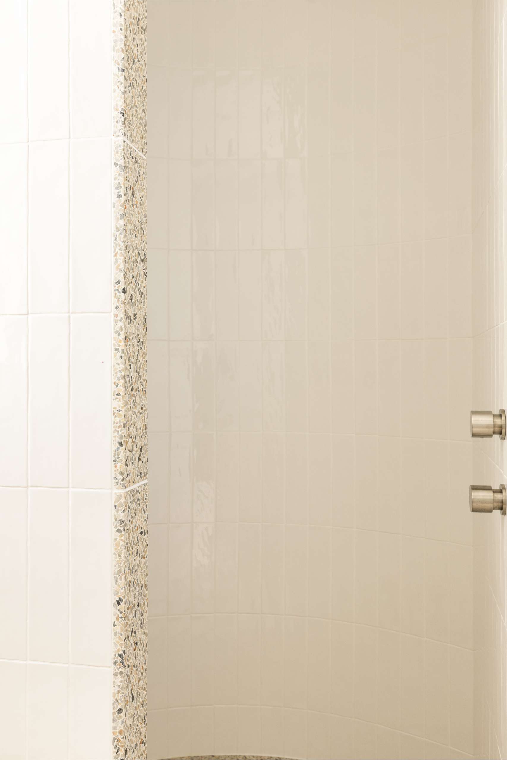 Soft curves and sculptural detail define this minimalist ensuite bathroom, where a terrazzo floor flows seamlessly into a curved walk-in shower. A soothing palette of white tile and natural textures completes the spa-like atmosphere.