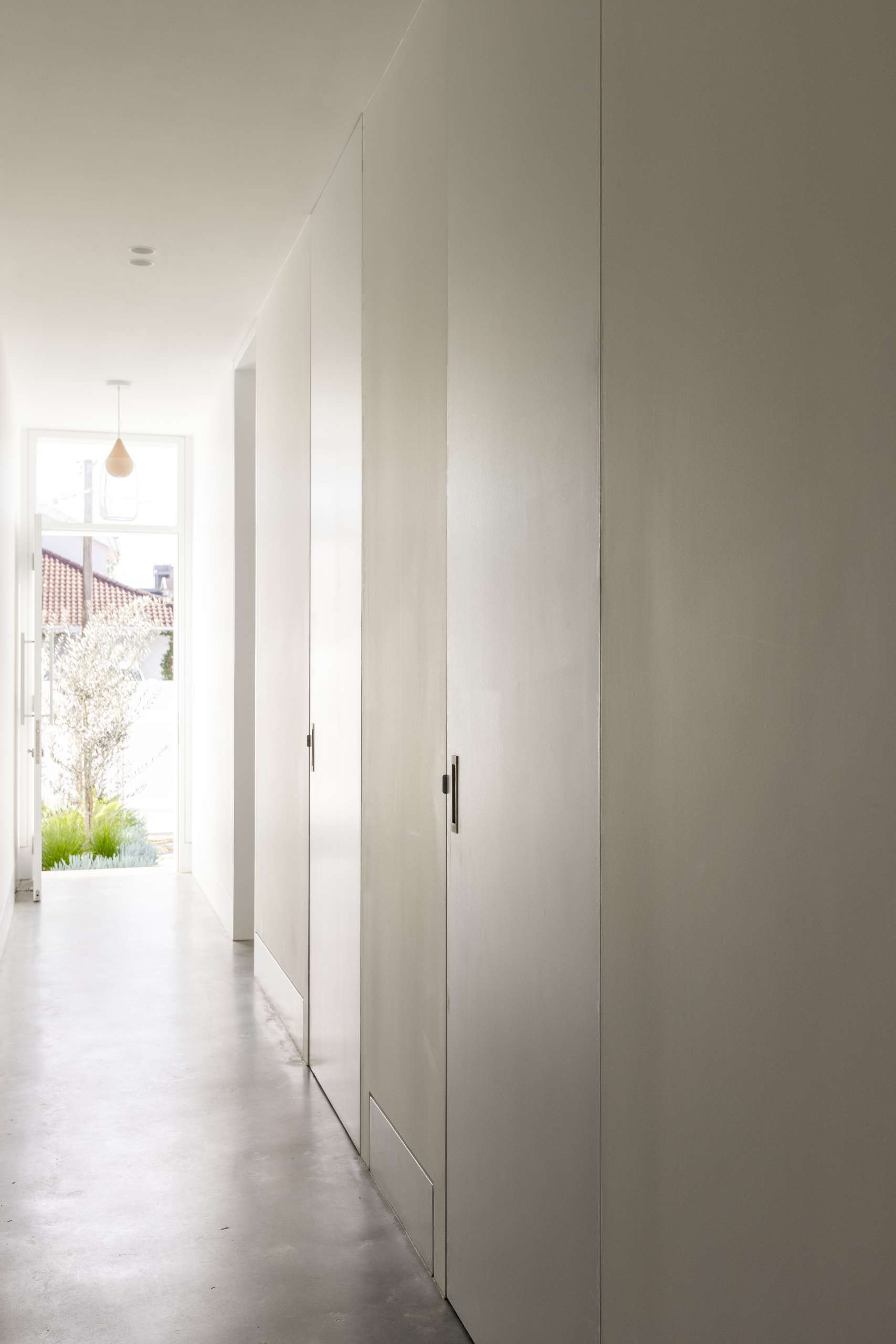 This serene hallway off the front door showcases a refined approach to minimalism, where full-height flush doors blend seamlessly into the wall to create a clean, sculptural surface. A compact study nook, kids’ playroom, and well-planned laundry sit discreetly off the hallway.