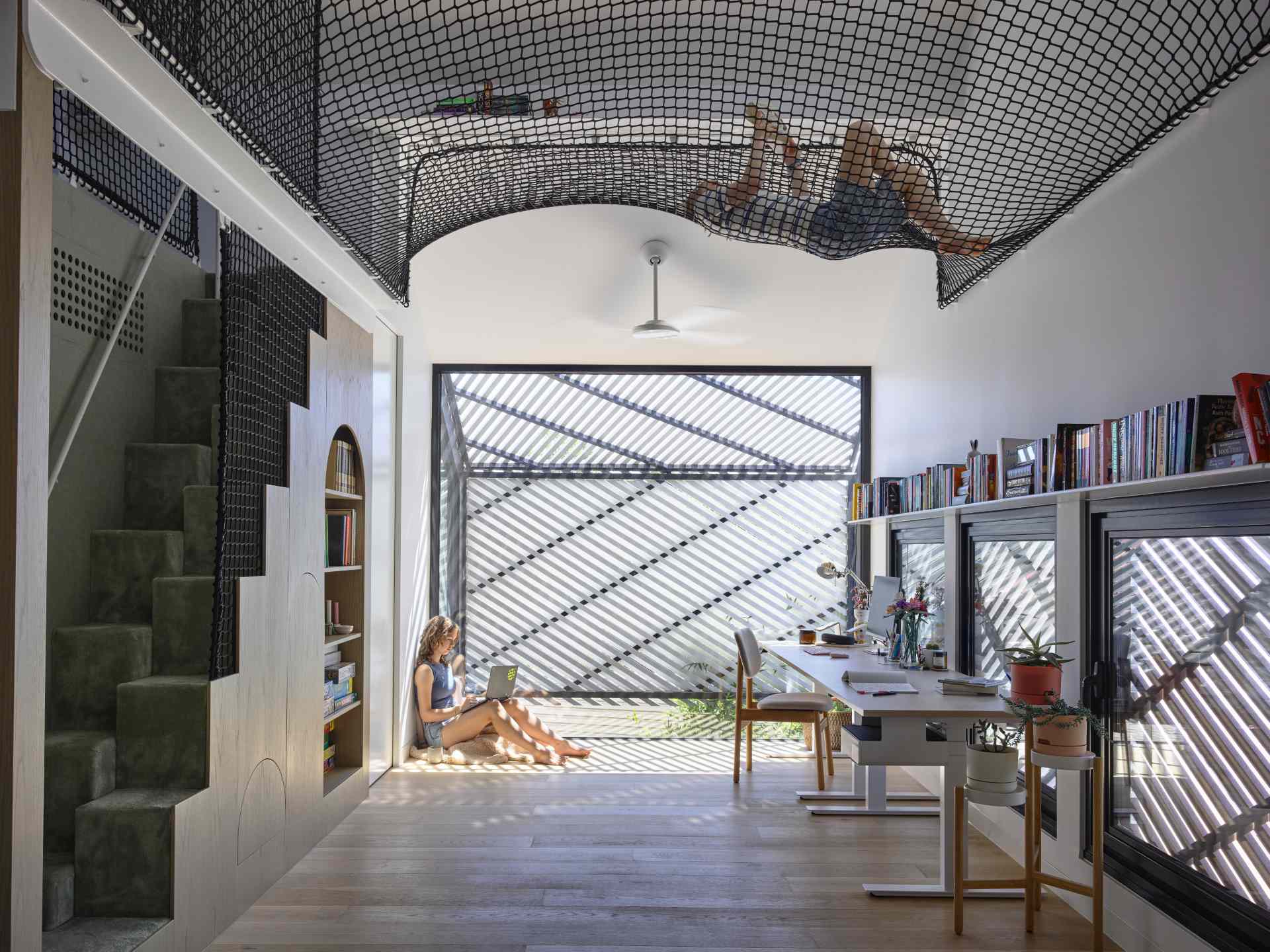 A contemporary loft area with a desk, bookshelves, and a hammock net.