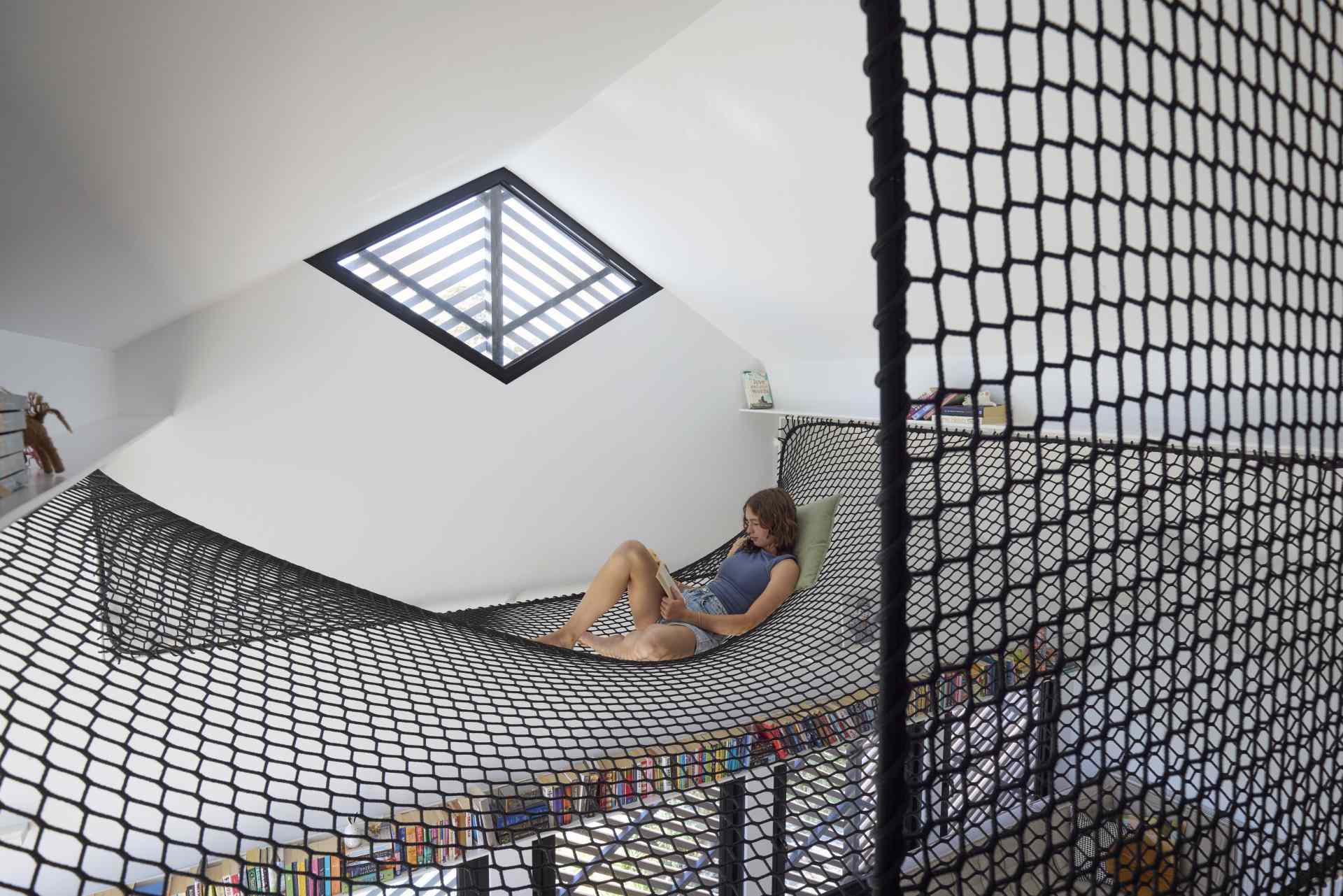 A contemporary loft area with a desk, bookshelves, and a hammock net.