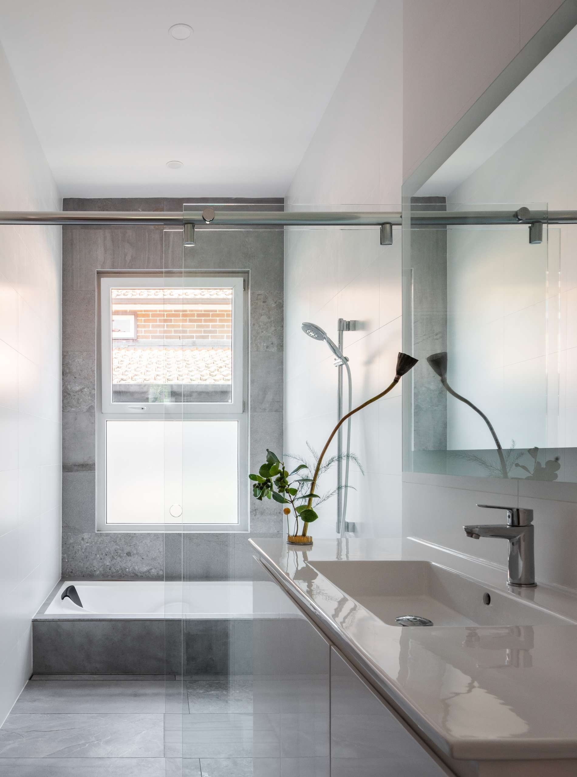 This bathroom pairs calm materials with precise detailing. Soft light filters through frosted glass, illuminating the stone and white finishes. A single ikebana arrangement adds a quiet, sculptural gesture that echoes the home’s connection to nature and simplicity.
