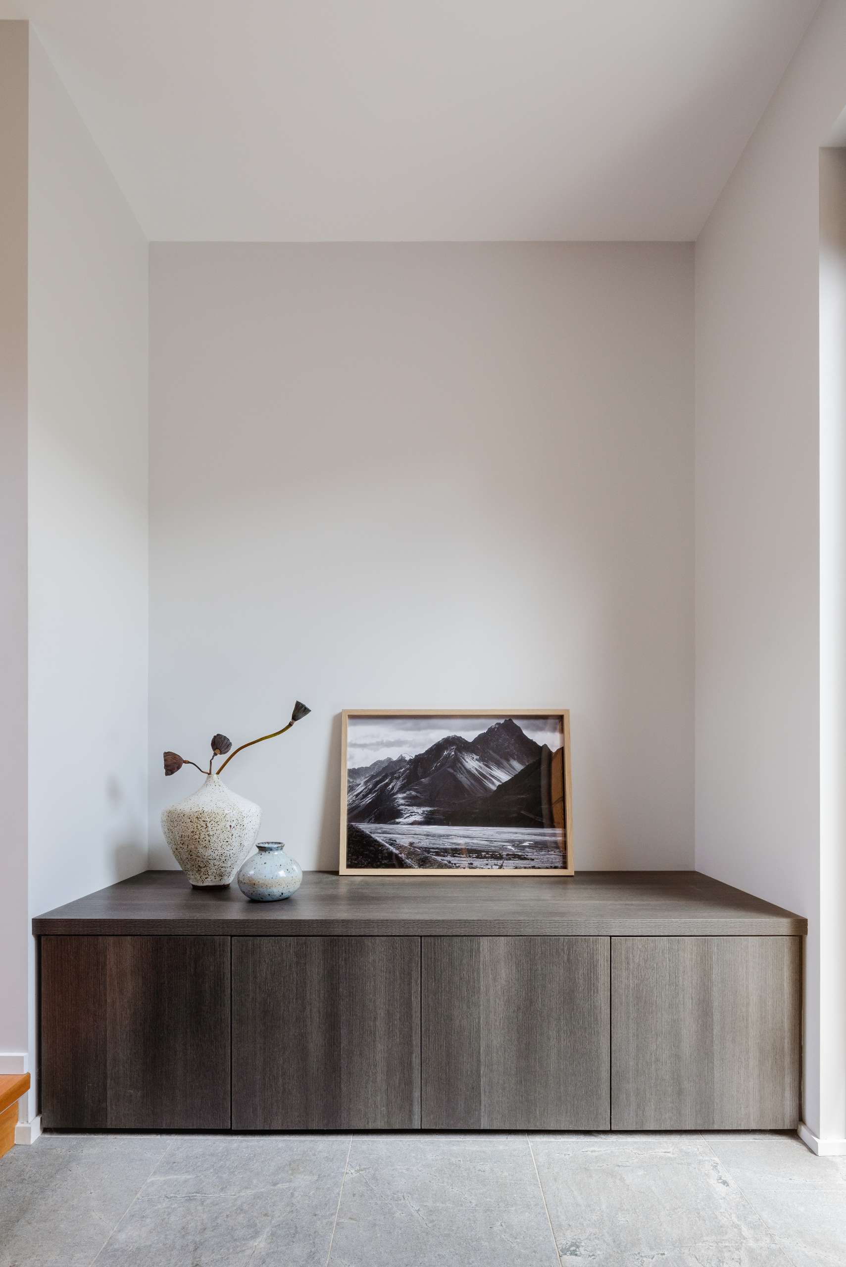 A quiet moment in the genkan, where dark timber joinery, cool stone tiles, and wabi-sabi ceramics create a calm, welcoming entry steeped in Japanese tradition.