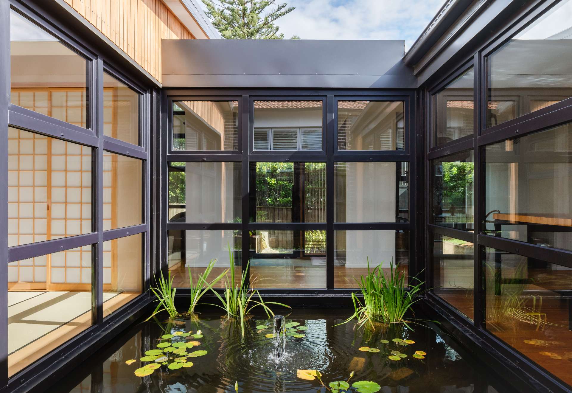 A tranquil courtyard reflection pond forms the serene heart of this home, framed by  black steel windows that invite nature into every room.