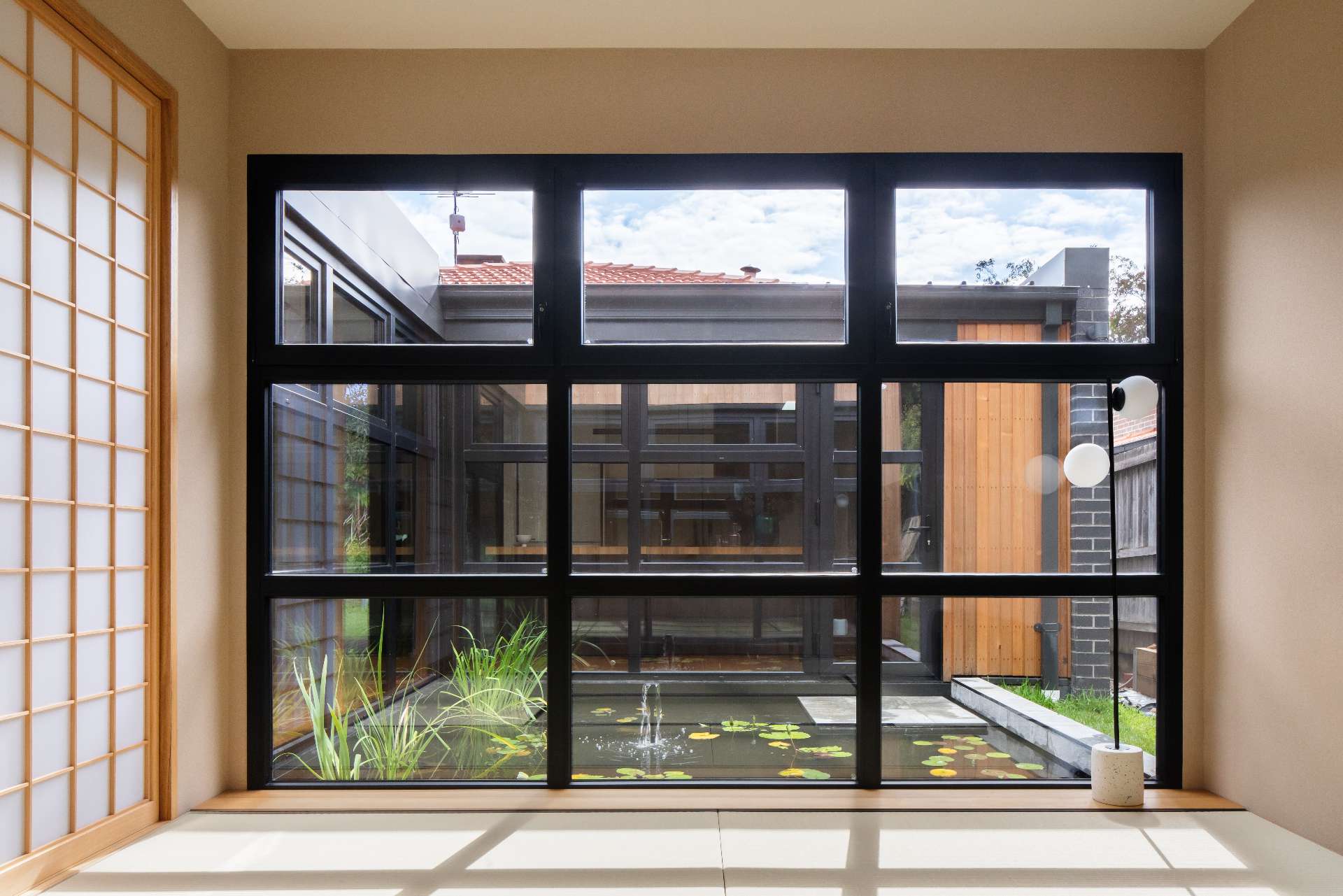 A tranquil courtyard reflection pond forms the serene heart of this home, framed by  black steel windows that invite nature into every room.