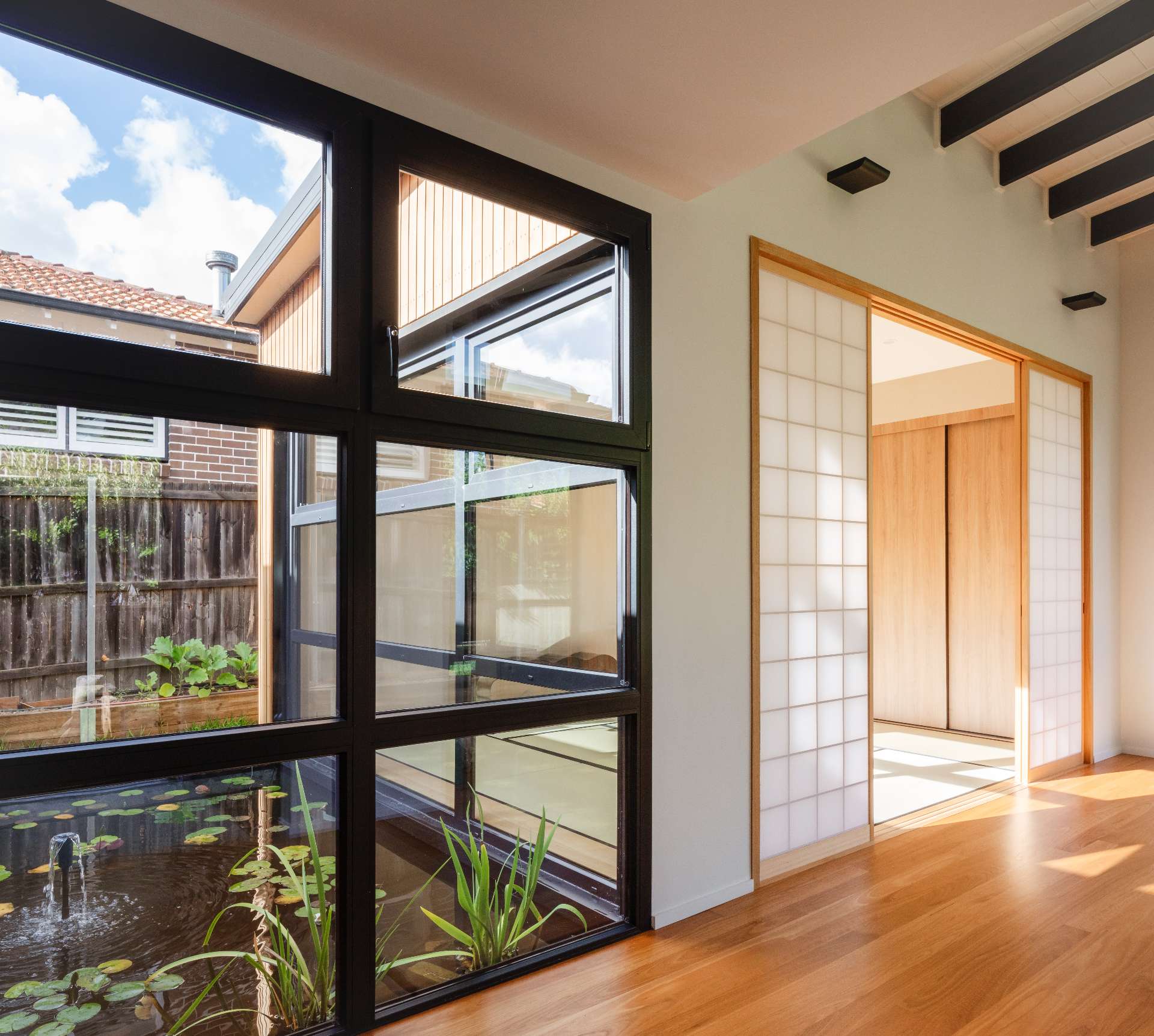 Natural light floods this hallway where shoji screens meet sleek black-framed windows, offering peaceful views of a reflection pond that anchors the home's Japanese-inspired design.