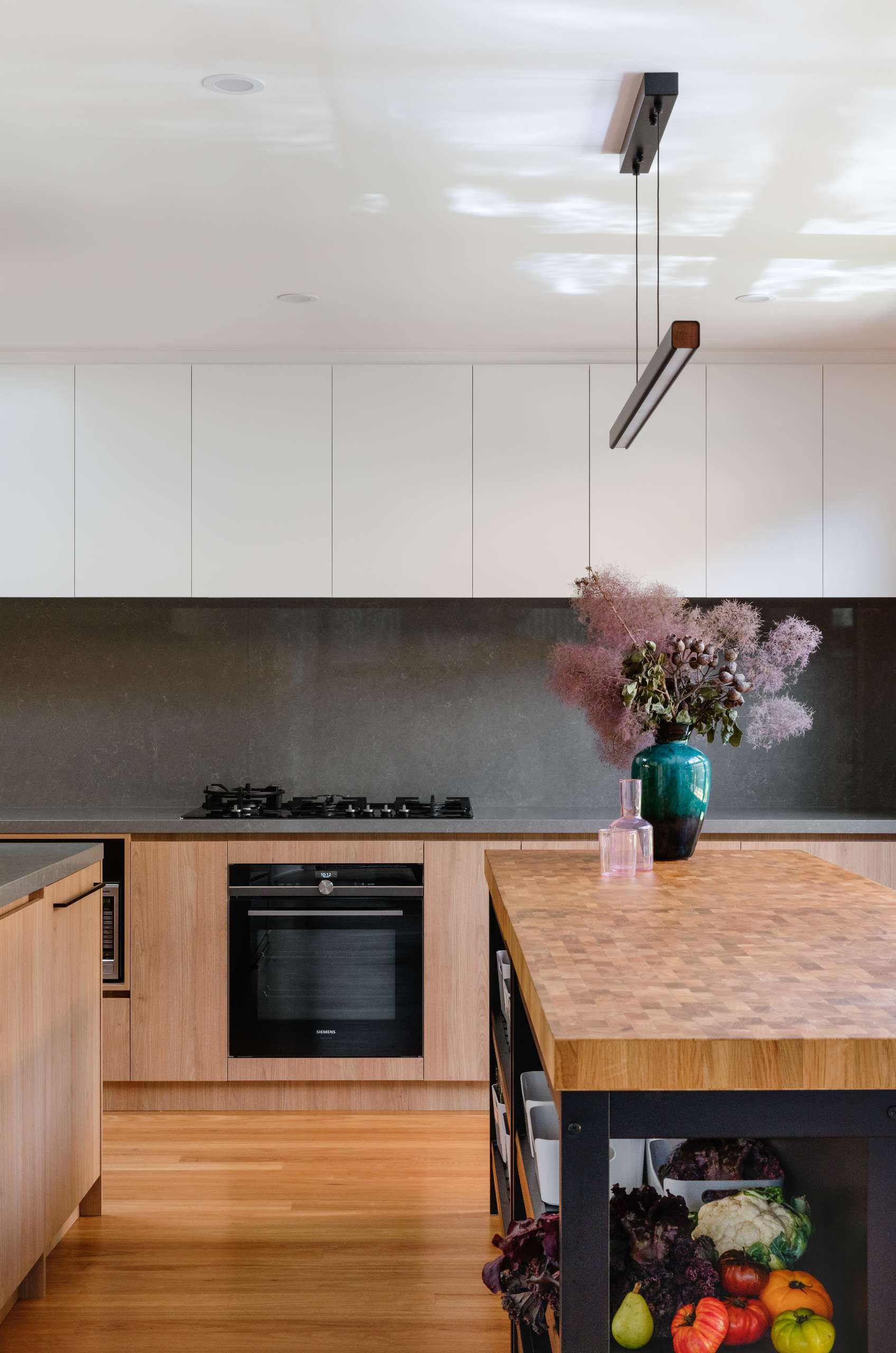 This Japanese-inspired kitchen has views of a tranquil reflection pond, blending natural textures with clean, modern lines. Black-framed windows flood the space with light, while the butcher-block island adds warmth and artisanal character.